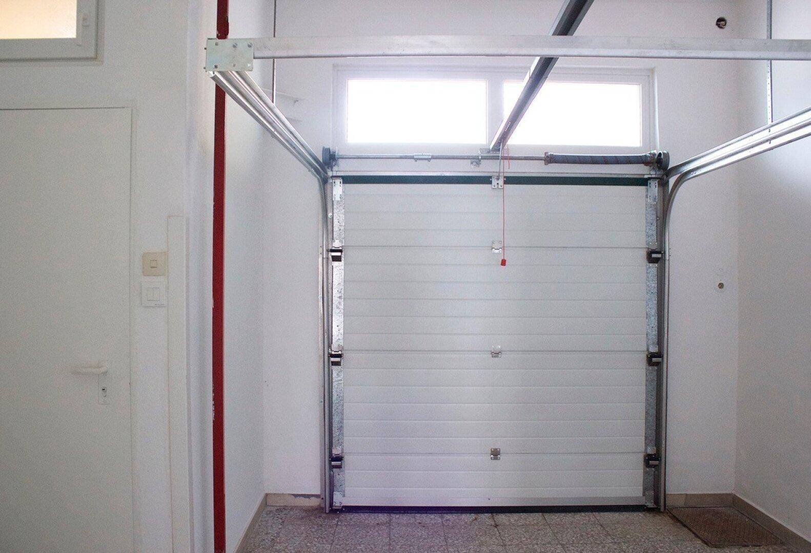 Innenansicht einer Garage mit weißem Rolltor und kleinen Fenstern für natürlichen Lichteinfall.