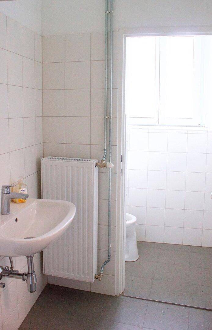 Einfaches Badezimmer mit Waschbecken, Heizkörper und weiß gefliesten Wänden, bereit zur Nutzung.