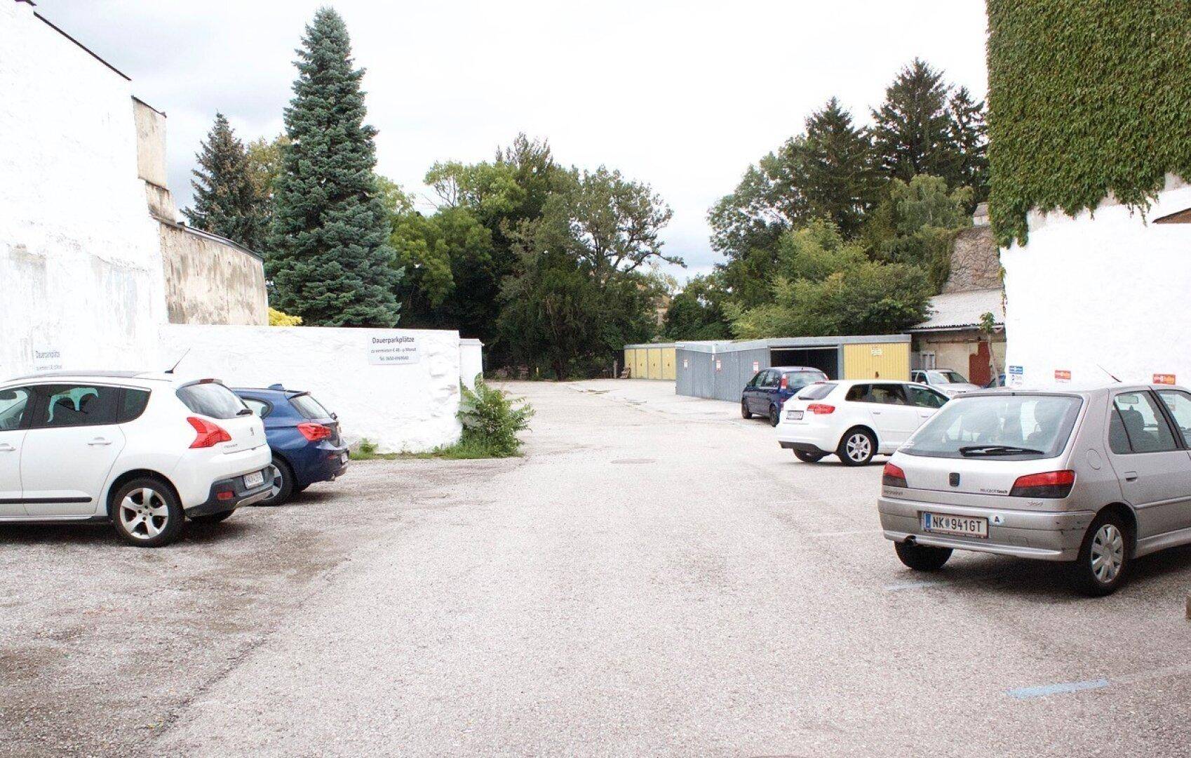 Großer Außenparkplatz mit mehreren geparkten Autos und viel Grün im Hintergrund der Bäume.