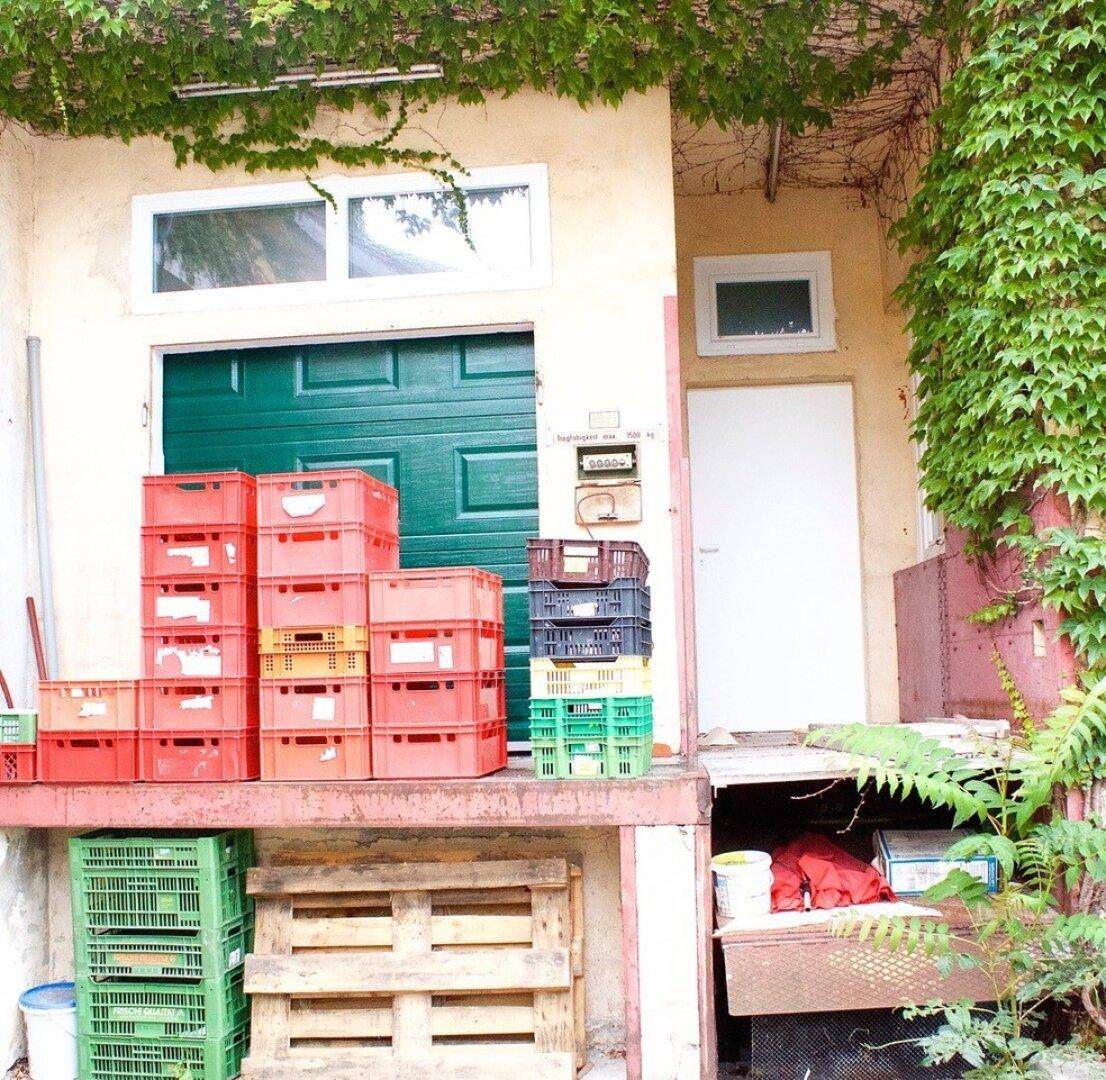 Laderampe mit grüner Tür und gestapelten Kisten, umgeben von Efeu an der Fassade.