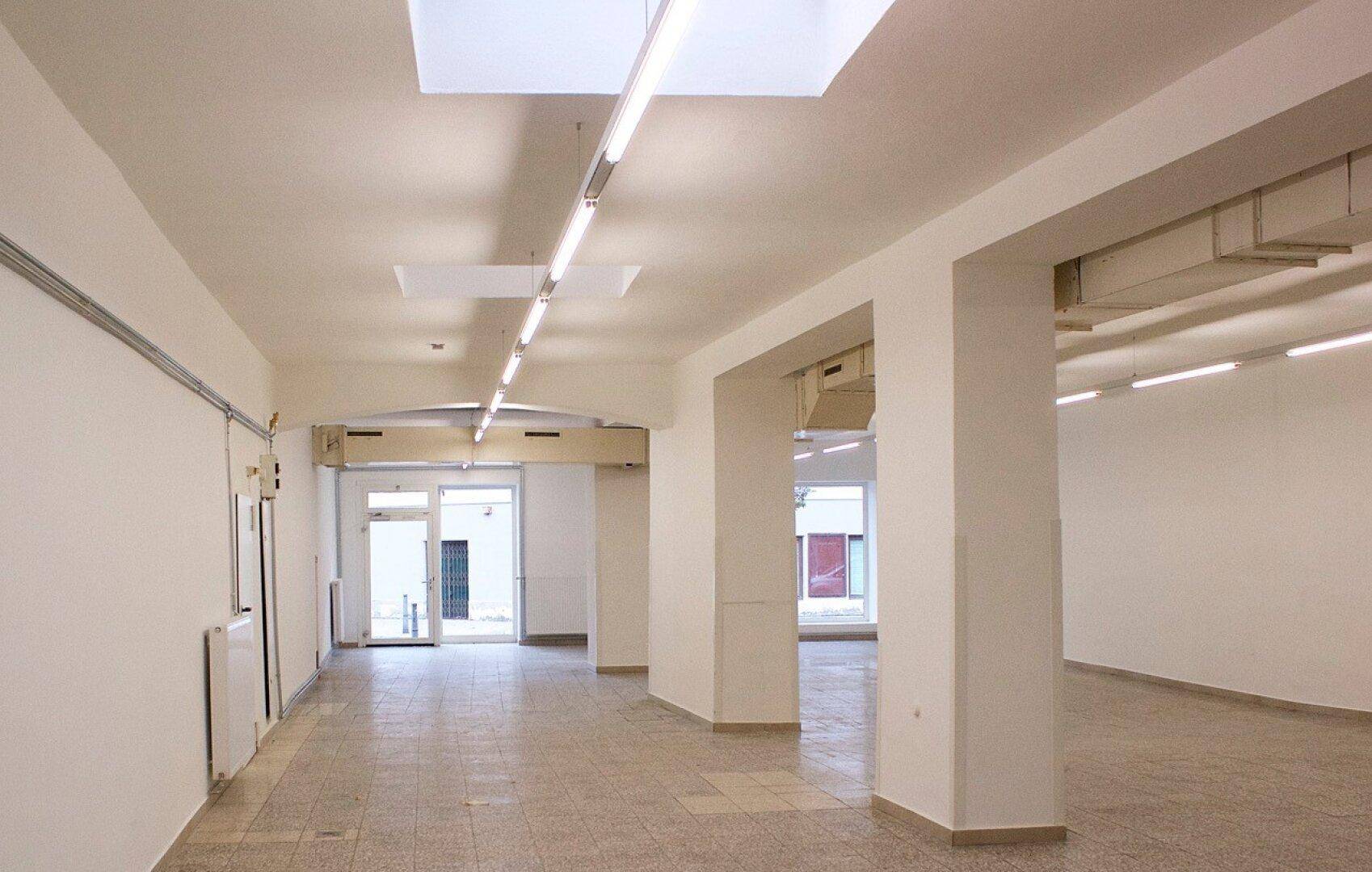Heller Gewerberaum mit Eingangsbereich, Säulen und Deckenfenstern, die Tageslicht hereinlassen.