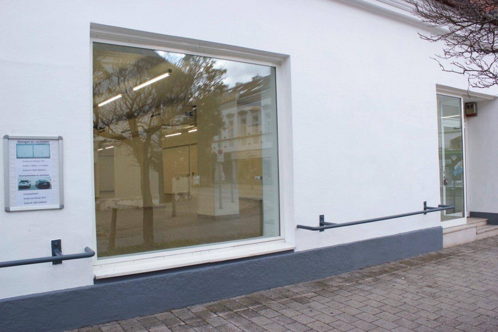 Nahaufnahme der weißen Fassade eines Geschäftsgebäudes mit einem großen Schaufenster und Reflexionen.