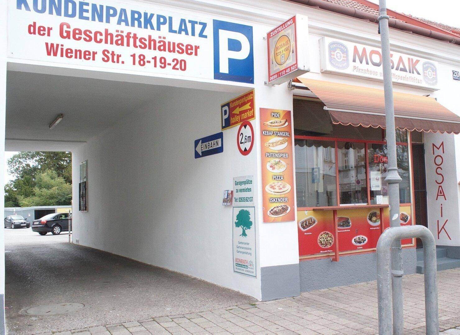Einfahrt zum Kundenparkplatz eines Geschäftsgebäudes mit Imbissstand und Hinweisschildern.