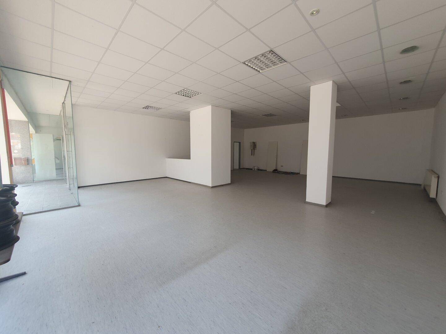 Offener Geschäftsraum mit Glasabtrennung, tragenden Säulen und viel Tageslicht.