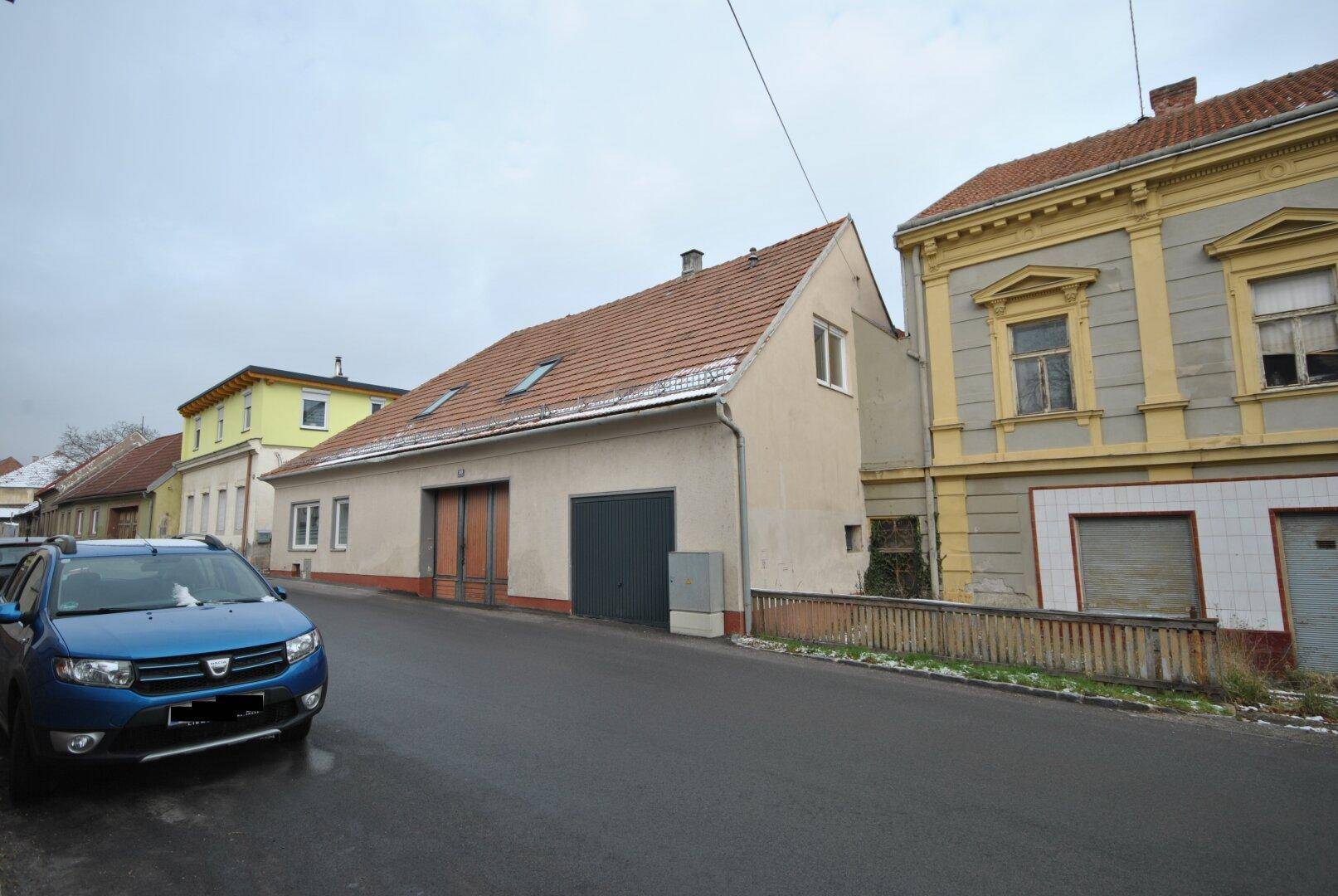 Ansicht eines Gebäudes mit Ziegeldach und Garagentoren von der Straße aus, mit Auto davor.
