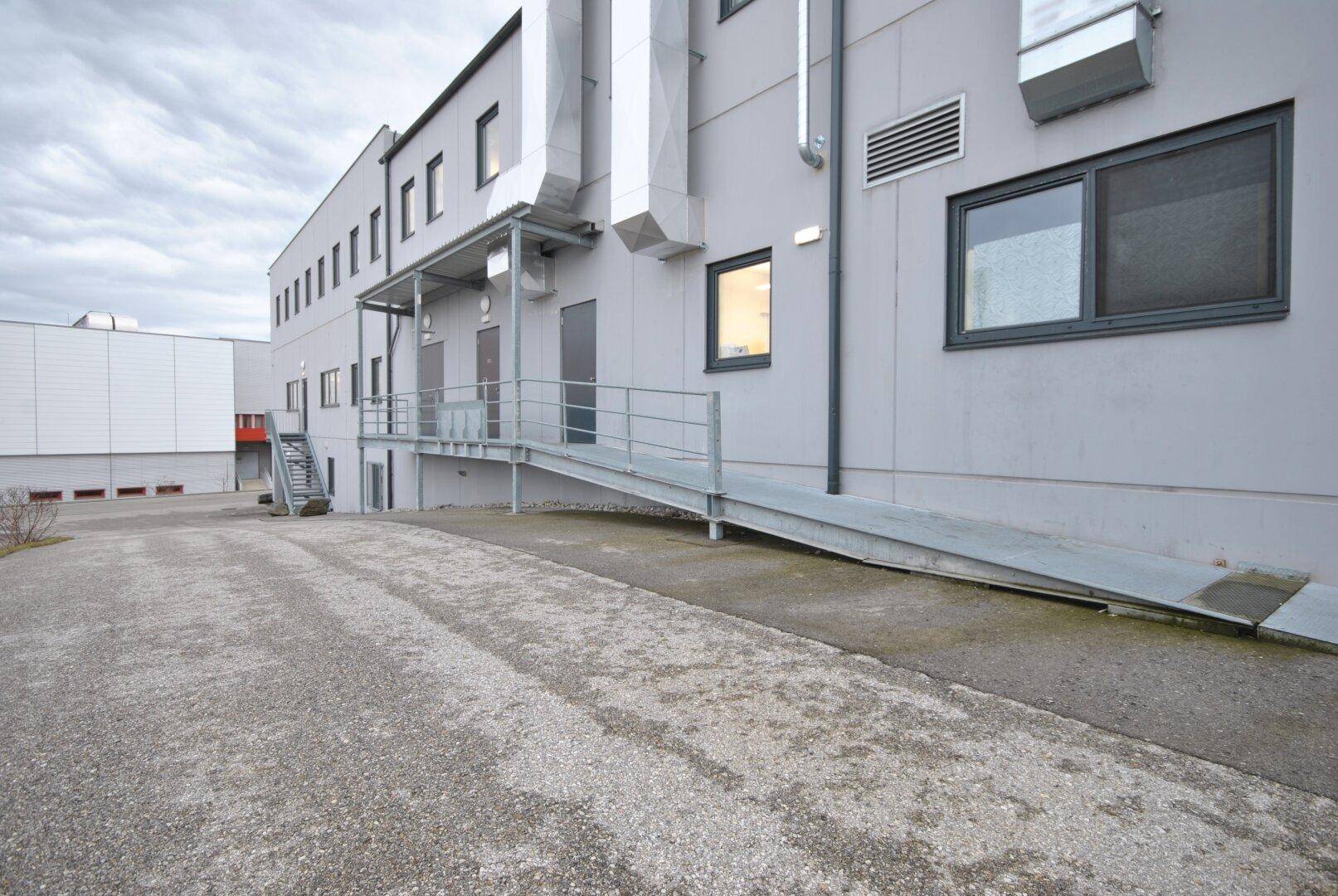 Moderne Gewerbegebäude-Fassade mit einer Zugangsrampe und großen Lüftungsrohren an der Außenseite.