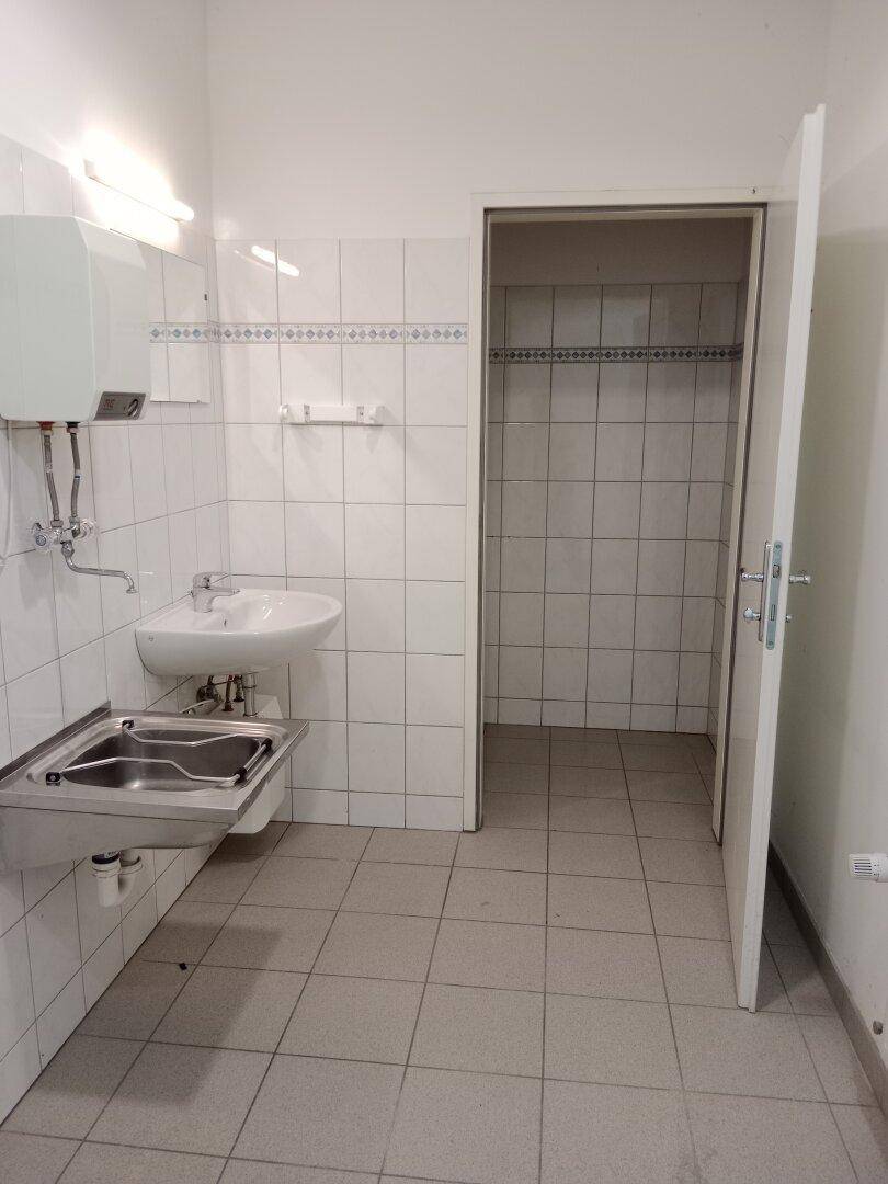 Kleiner Waschraum oder Abstellraum mit weißen Wandfliesen, einem Waschbecken und einem Edelstahlwaschtrog.