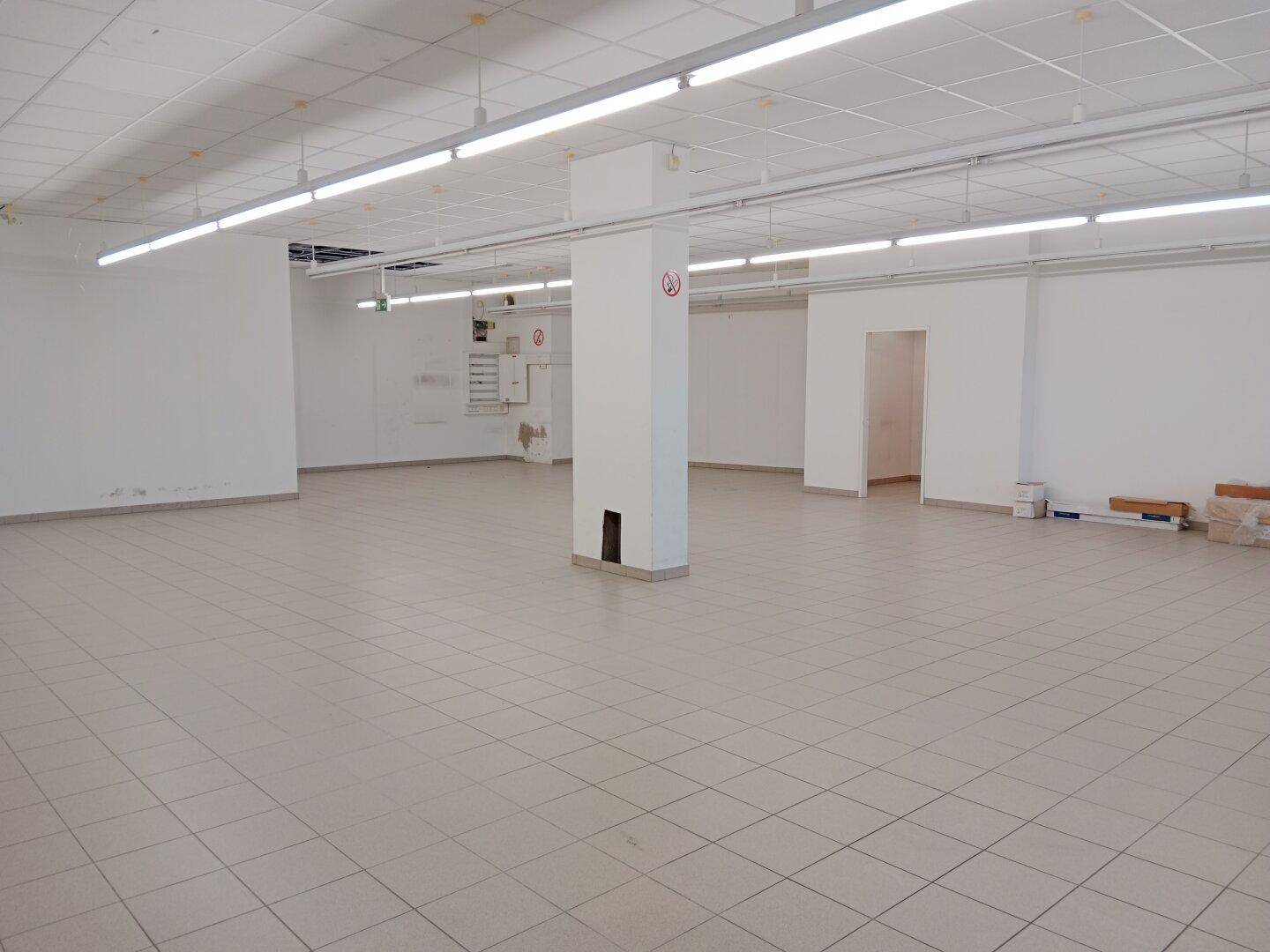 Weitläufiger, heller Geschäftsraum mit Fliesenboden, einer zentralen Säule und einer Rasterdecke mit Beleuchtung.