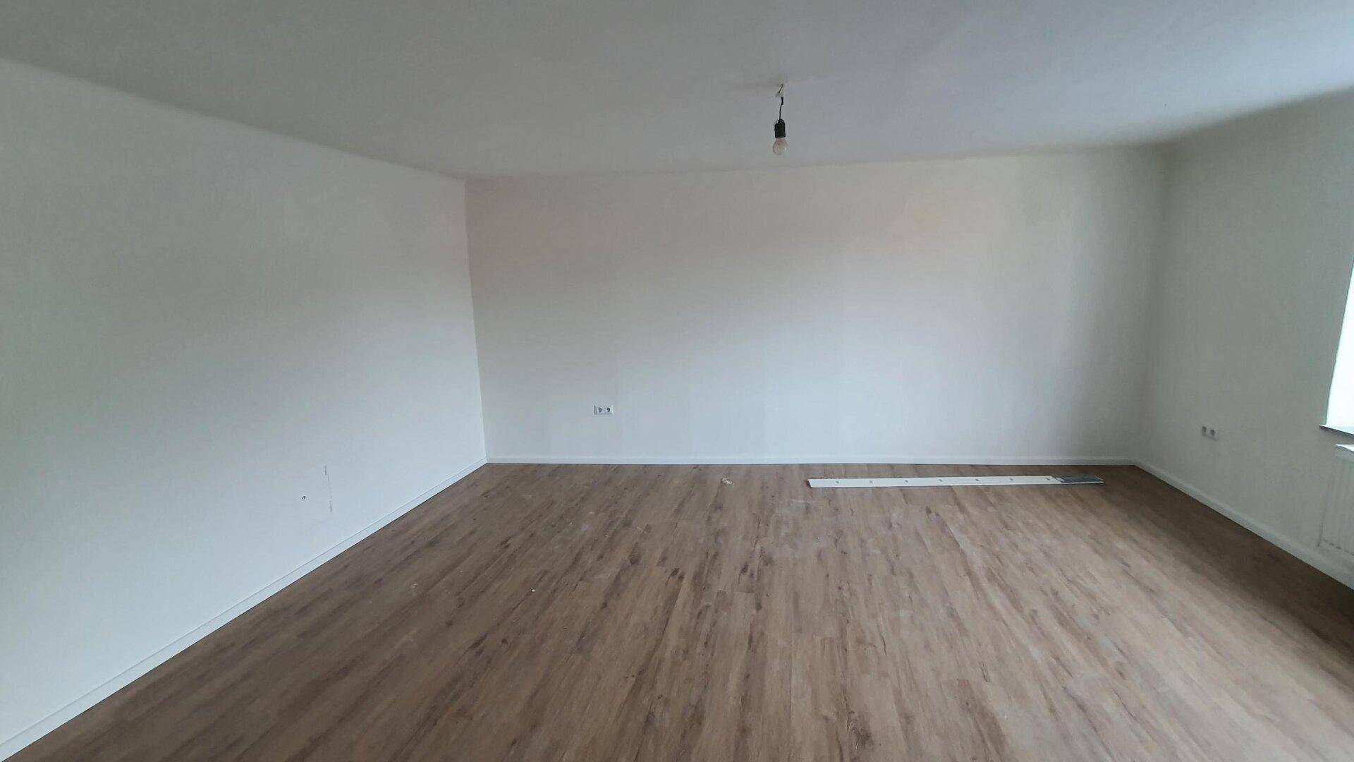 Heller, leerer Raum mit neuem Laminatboden und frisch gestrichenen weißen Wänden.