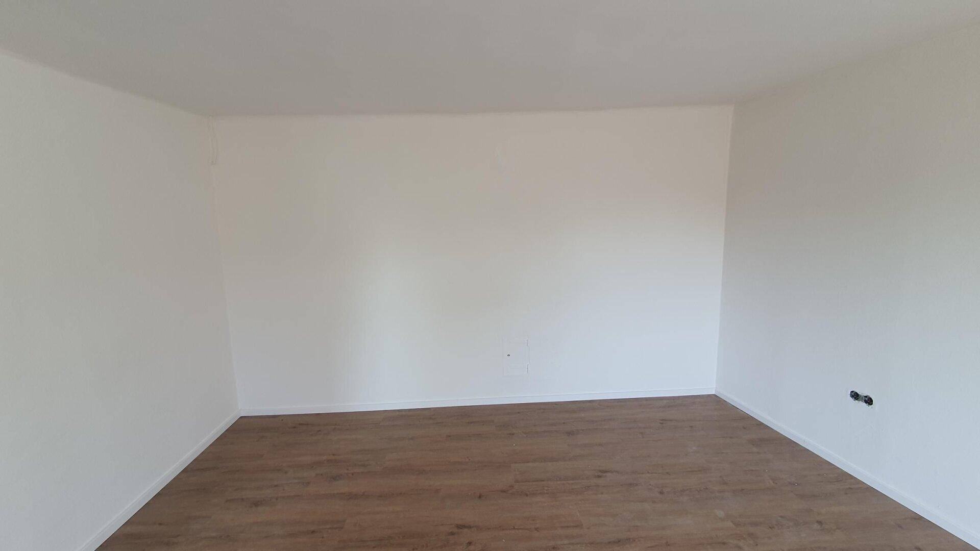 Sauberer, leerer Raum mit Laminatboden und weißen Wänden, ideal für individuelle Gestaltung.