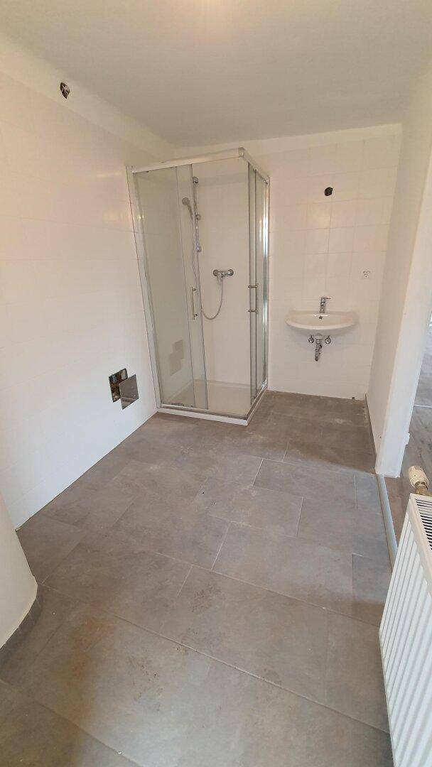 Modernes Badezimmer in Renovierung mit Duschkabine, Waschbecken und Heizkörper.