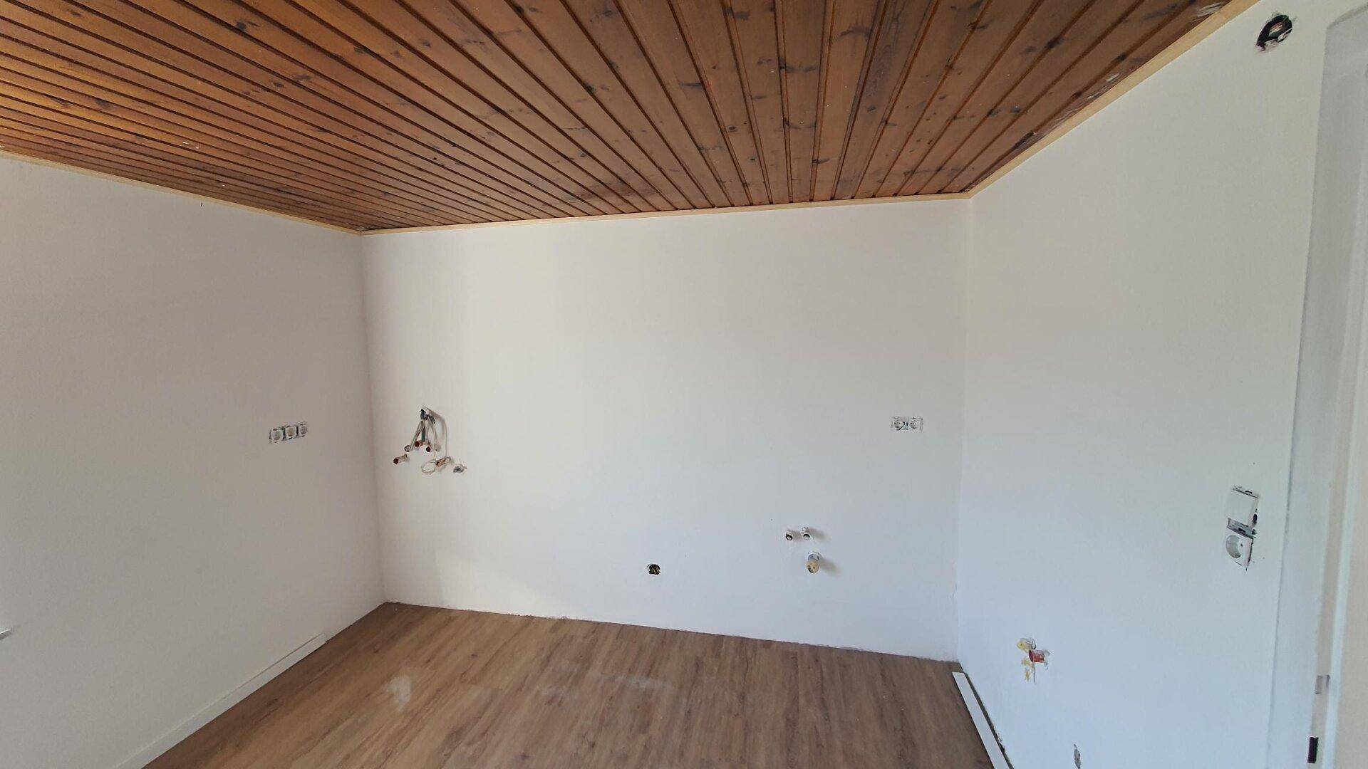 Raum mit Holzdeckenverkleidung und Laminatboden, vorbereitet für Sanitärinstallationen.