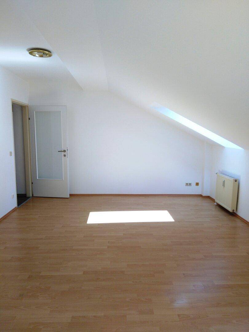 Heller Raum im Dachgeschoss mit Laminatboden, Dachschräge und Dachfenster.