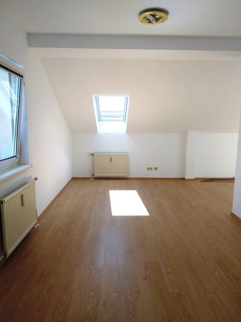 Lichtdurchfluteter Raum mit Laminatboden, Dachschräge und großem Dachfenster.