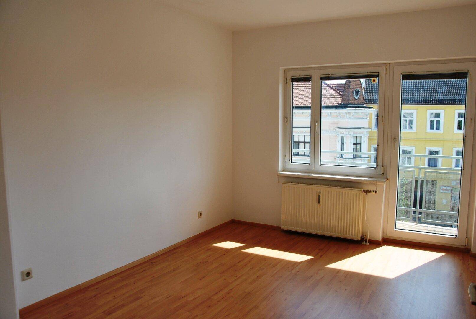 Heller Raum mit Laminatboden und Zugang zu einem französischen Balkon mit Stadtblick.