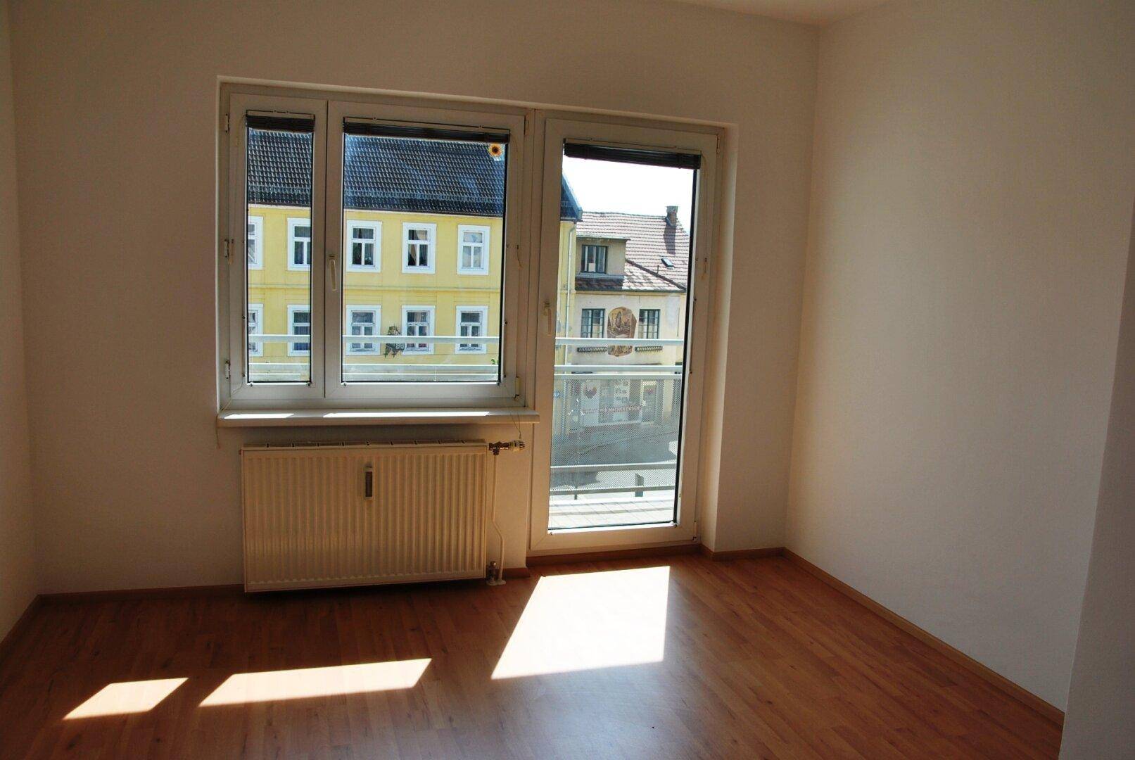 Lichtdurchfluteter Raum mit Laminatboden und Zugang zu einem französischen Balkon.