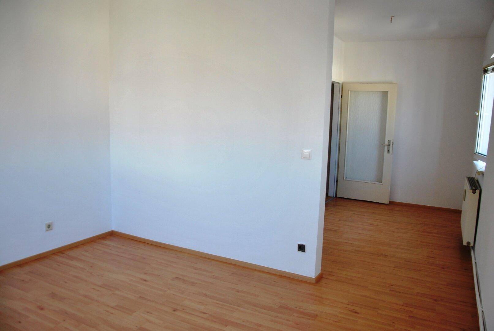 Leerer Raum mit Laminatboden und weiß gestrichenen Wänden, bereit zur individuellen Gestaltung.