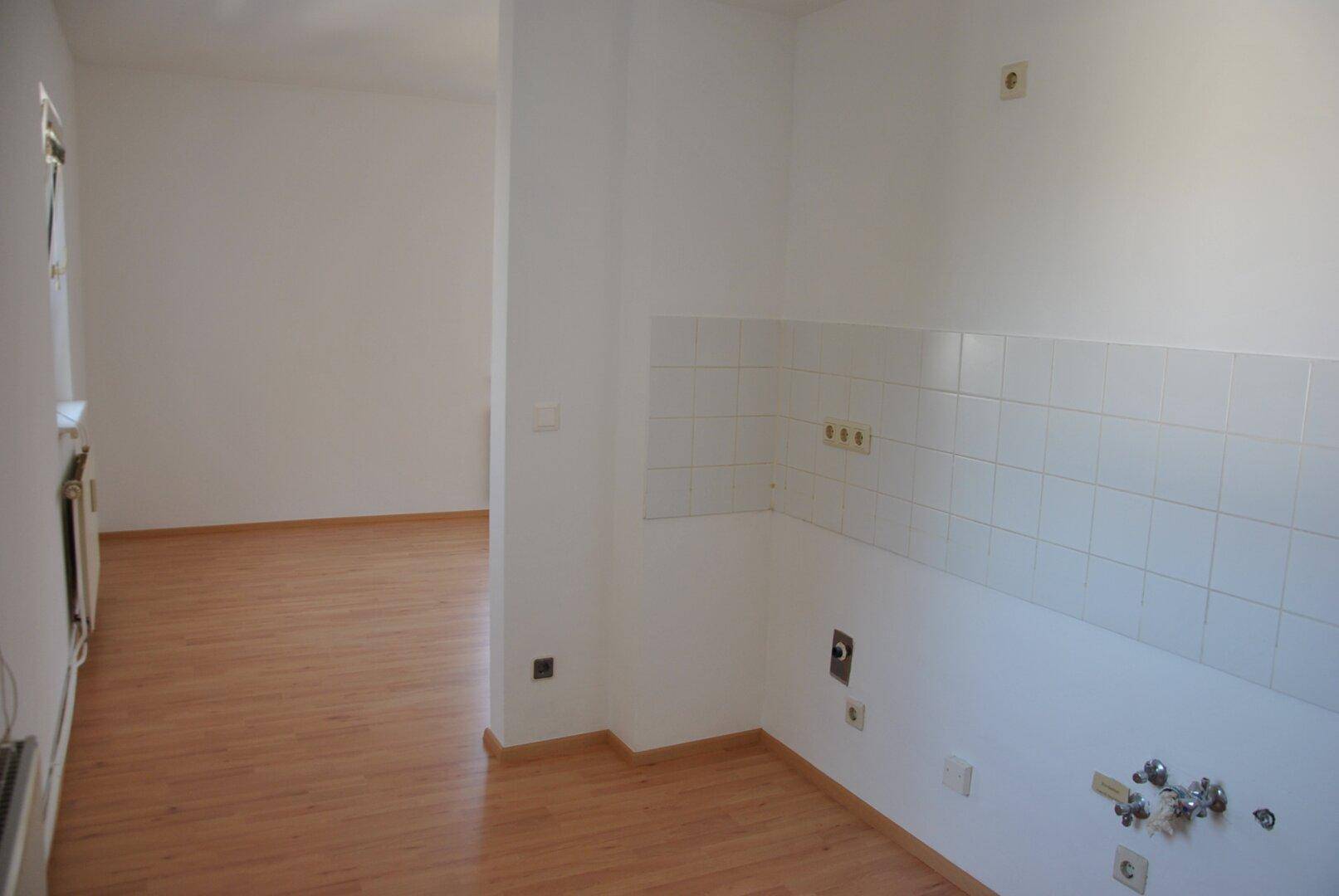 Leerer Küchenbereich mit Fliesenrückwand und Anschlüssen für eine zukünftige Einbauküche.