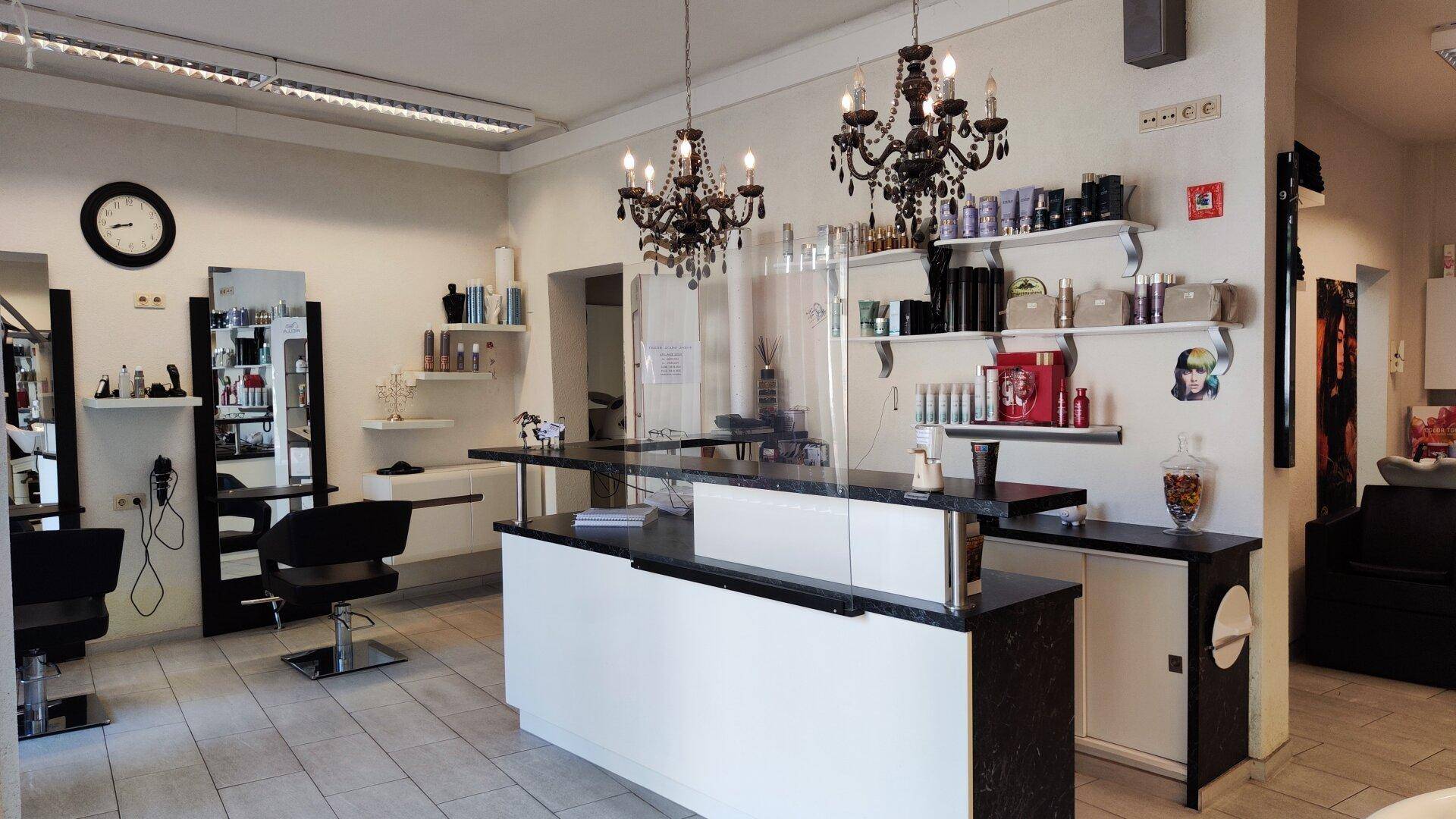 Empfangsbereich eines Friseursalons mit Theke, Kronleuchtern und Regalen voller Produkte.