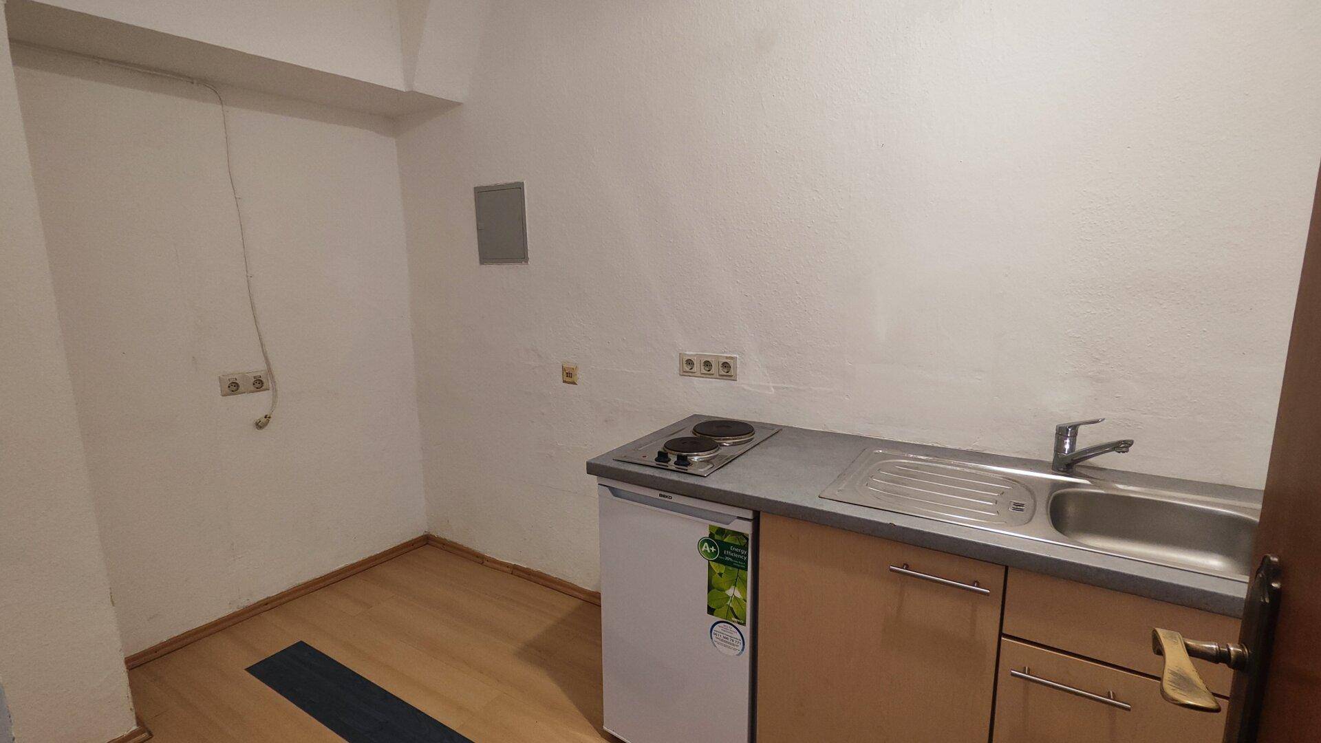 Eine kleine Küchenzeile mit Spüle, Kochplatten und Kühlschrank in einem einfachen, funktionalen Raum.