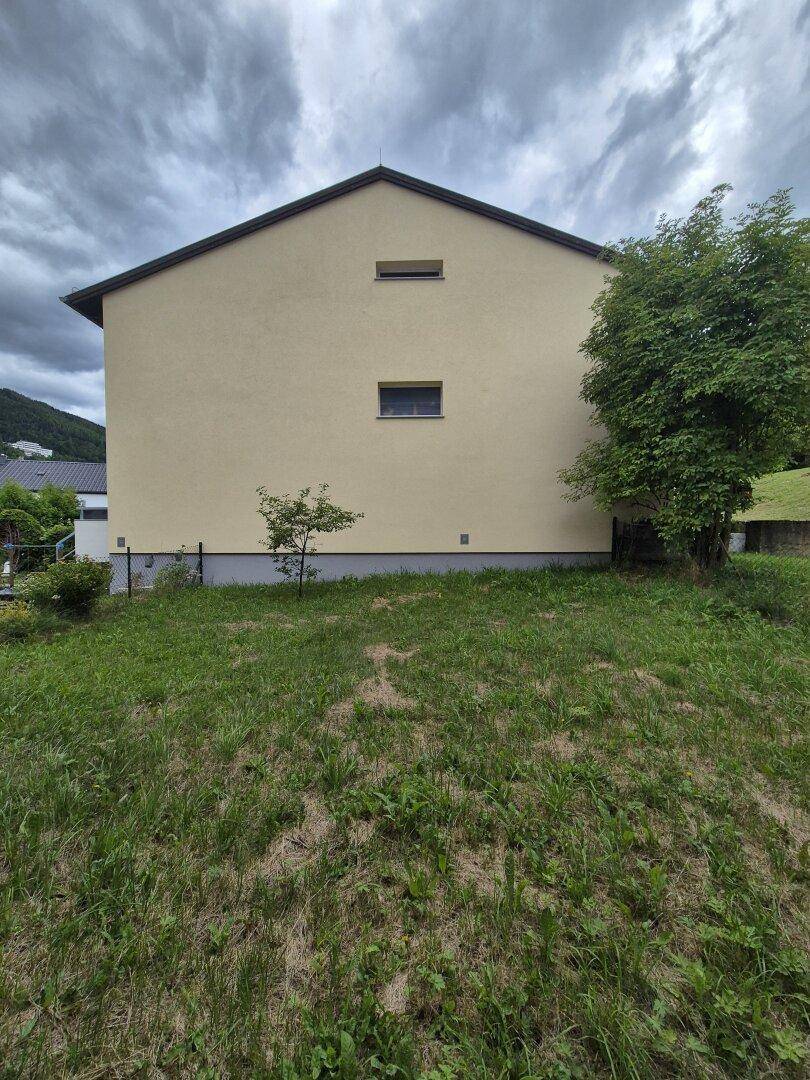 Seitenansicht eines Wohngebäudes mit schlichter Fassade und umliegender Grünfläche.