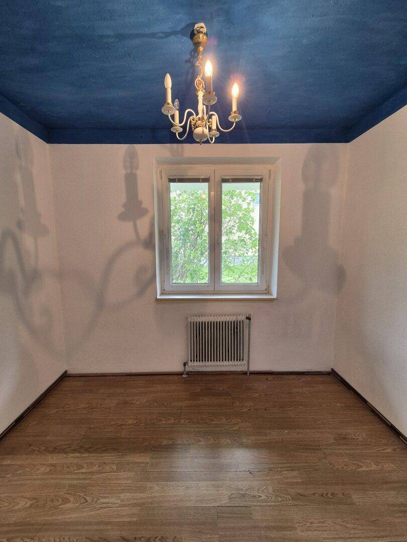 Zimmer mit auffälliger blauer Decke, Laminatboden und Fenster mit Blick ins Grüne.