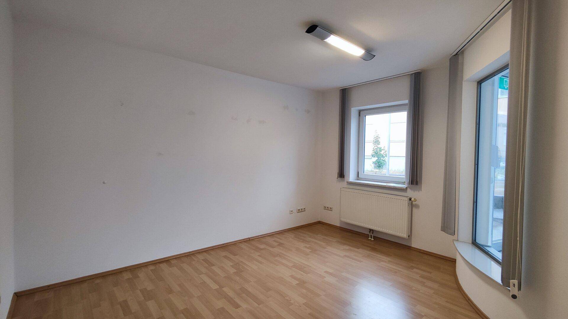 Leerer Büroraum mit Holzboden und großen Fenstern, die für viel natürliches Licht sorgen.