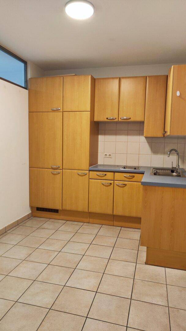 Funktionale Küche mit Holzschränken, Fliesenboden und einer Arbeitsplatte mit Spüle, bereit zur Nutzung.