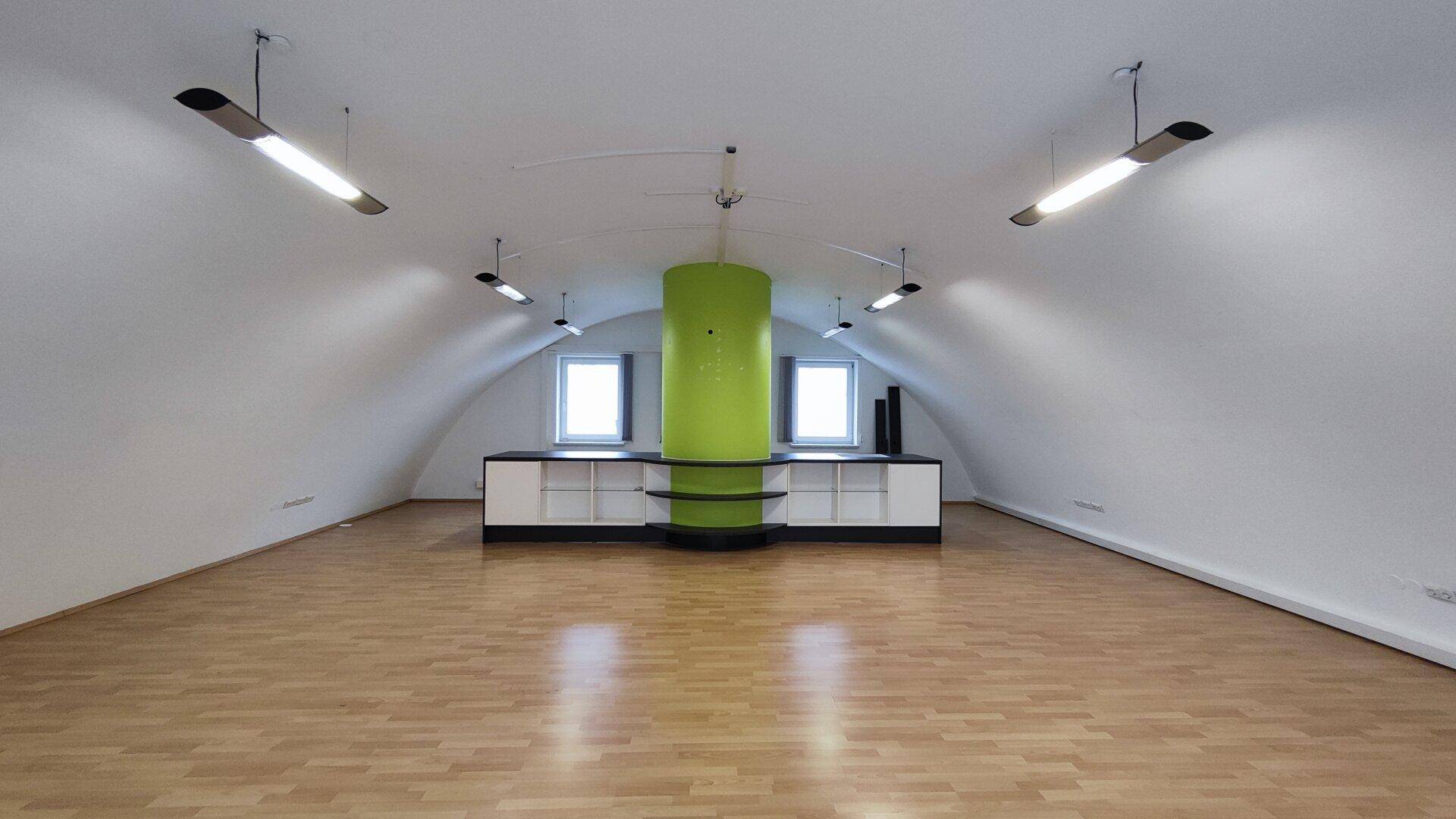 Großer offener Raum mit gewölbter Decke, Holzboden und einer auffälligen grünen Säule in der Mitte.