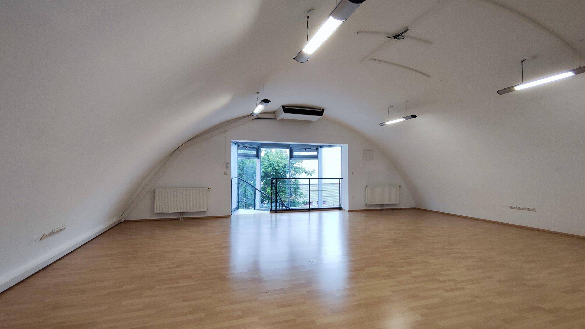 Geräumiger Loft-Raum mit gewölbter Decke, Holzboden und Blick auf den Eingangsbereich mit Wendeltreppe.