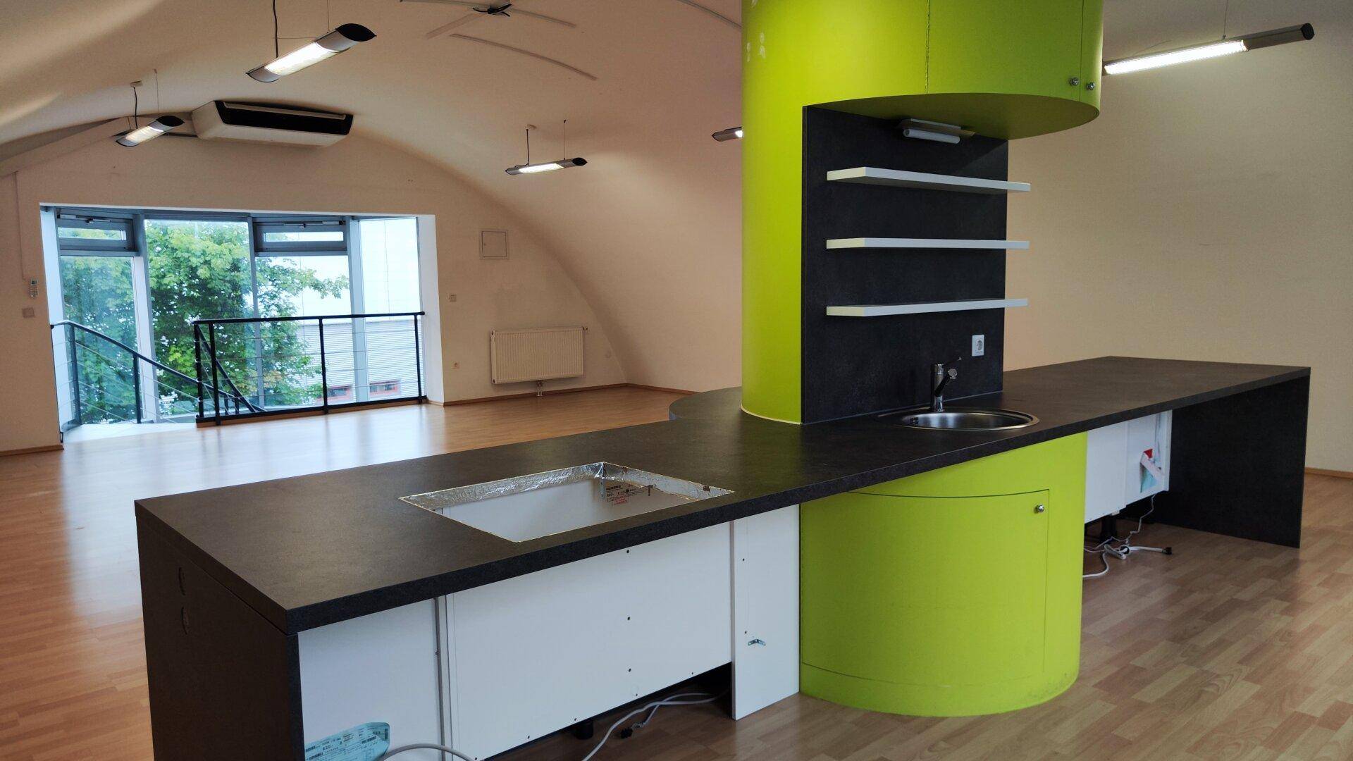 Moderne Küchenzeile mit grüner Säule, dunkler Arbeitsplatte und Spüle in einem offenen Loft-Raum.
