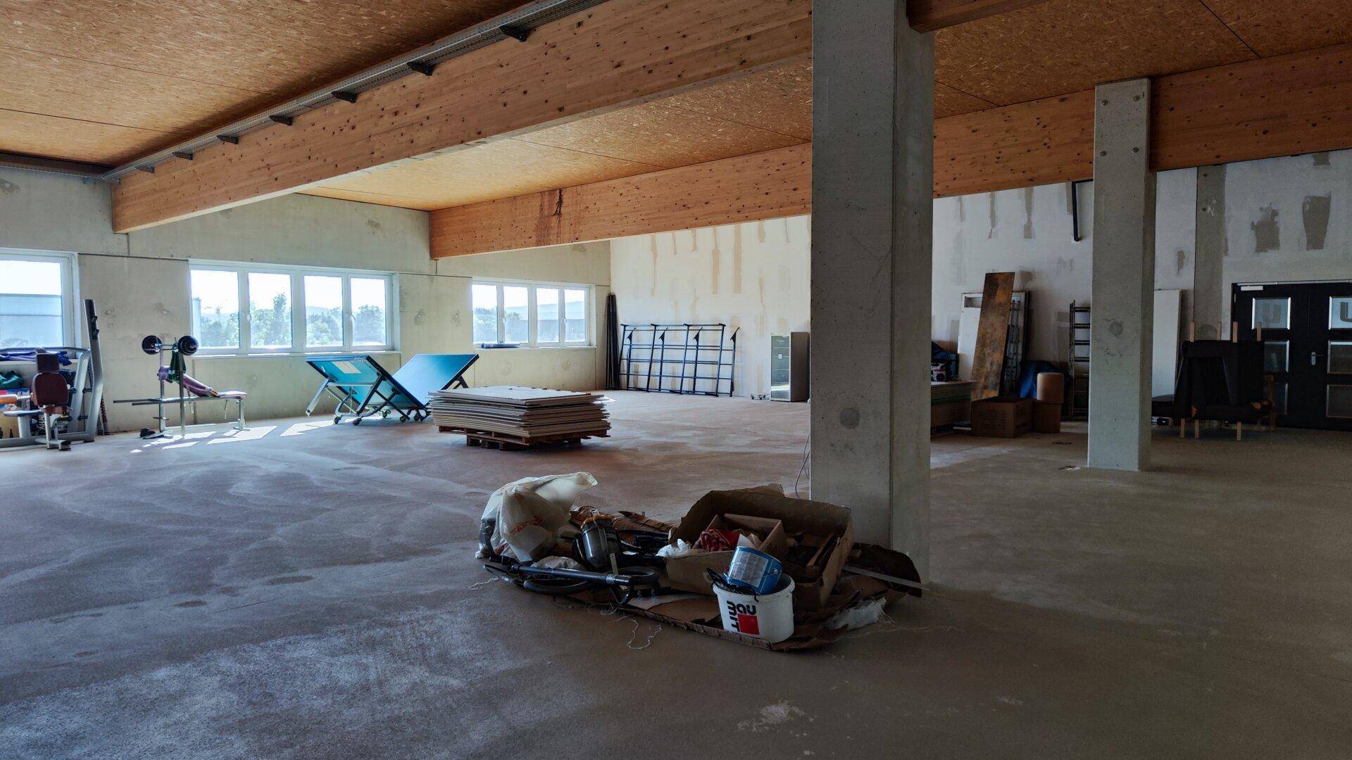 Geräumiger Gewerberaum im Rohzustand mit sichtbaren Holzbalken und großen Fenstern, ideal für individuelle Gestaltung.