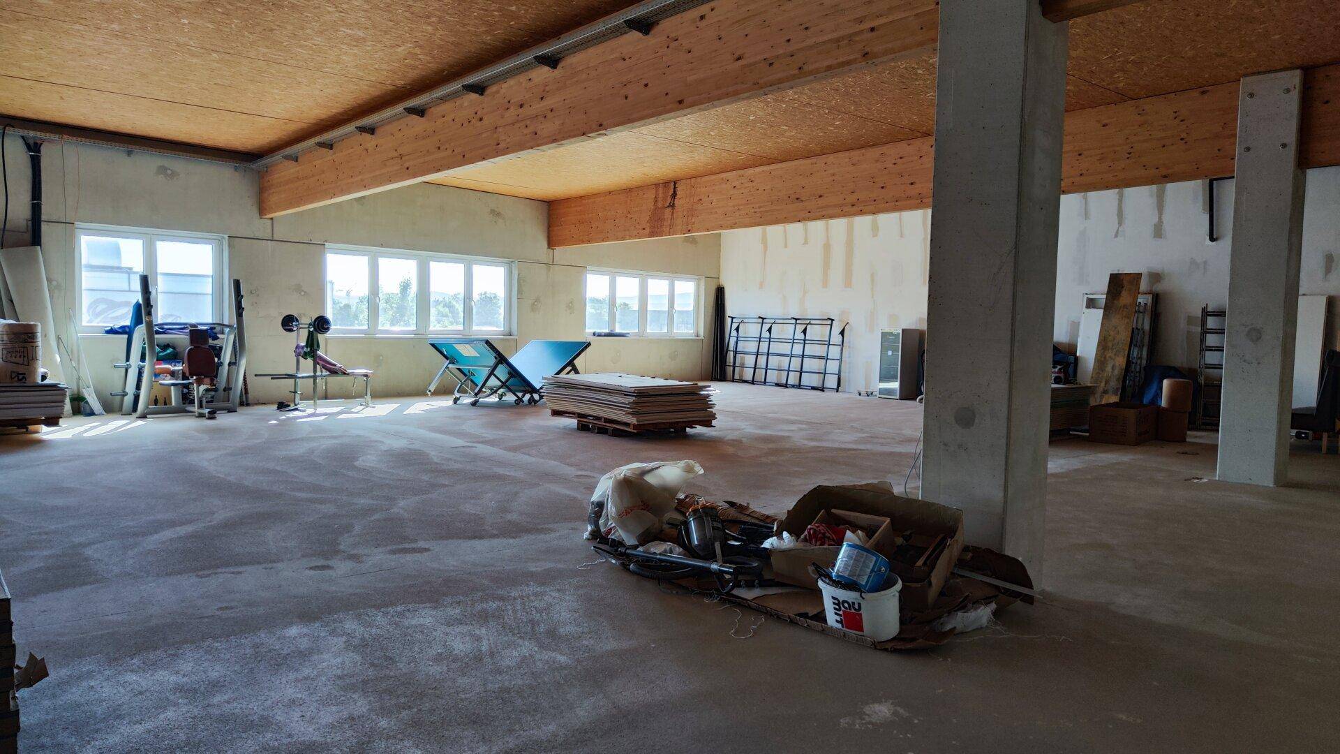 Heller Gewerberaum mit hoher Decke, Holzbalken und Betonboden, bereit für den Innenausbau und individuelle Nutzung.