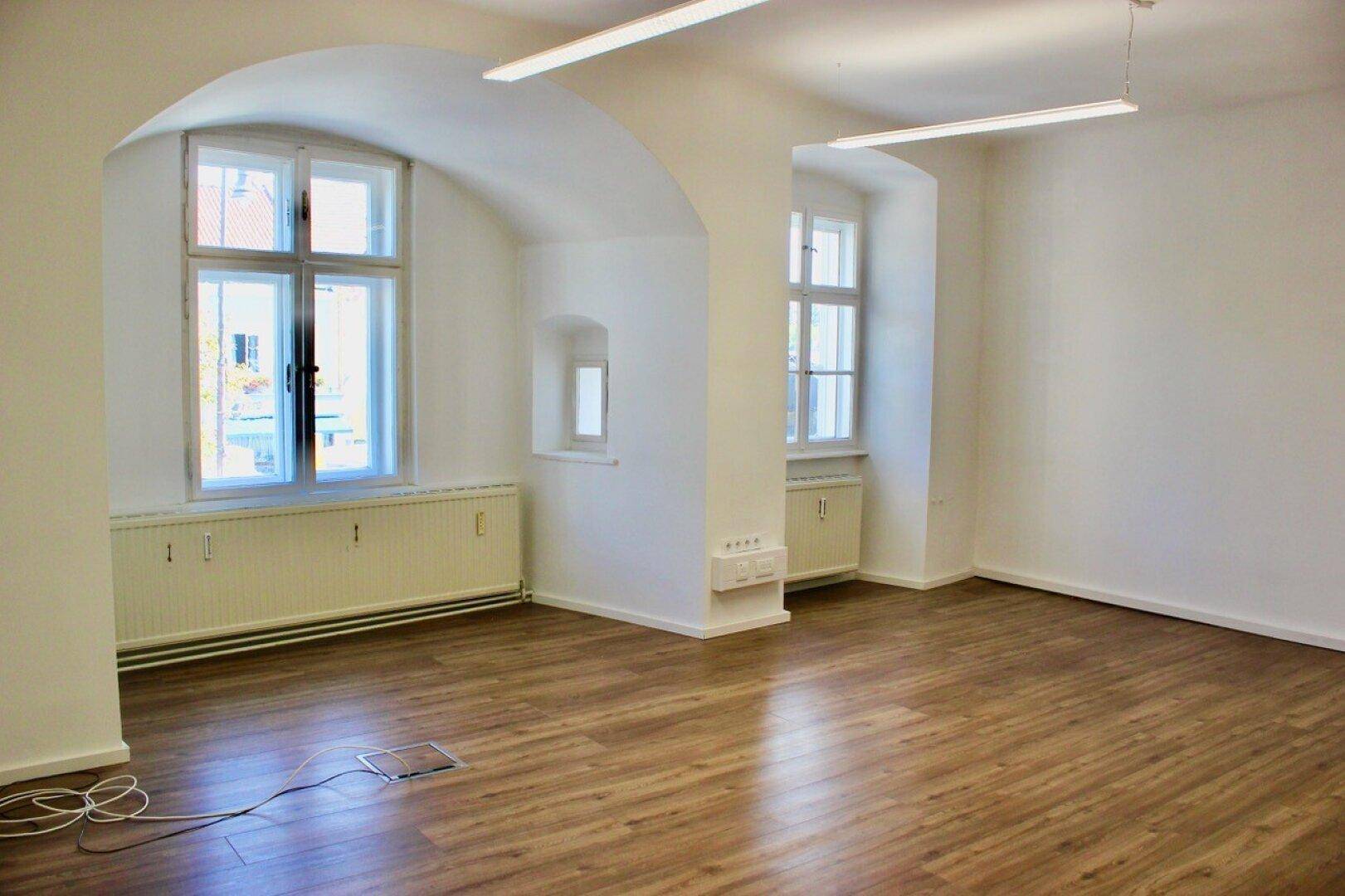 Heller Raum mit gewölbter Decke, großen Fenstern und Laminatboden, ideal für Büro oder Wohnen.