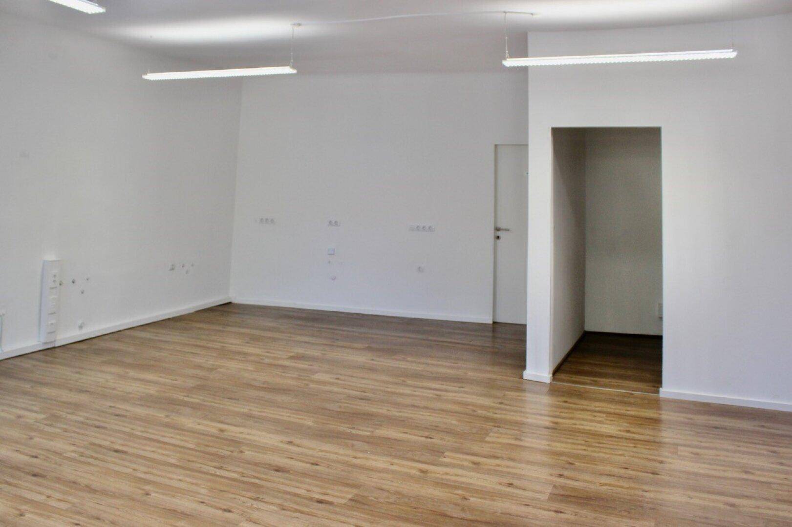 Leerer Raum mit hellem Laminatboden und weißen Wänden, bereit für individuelle Gestaltung.