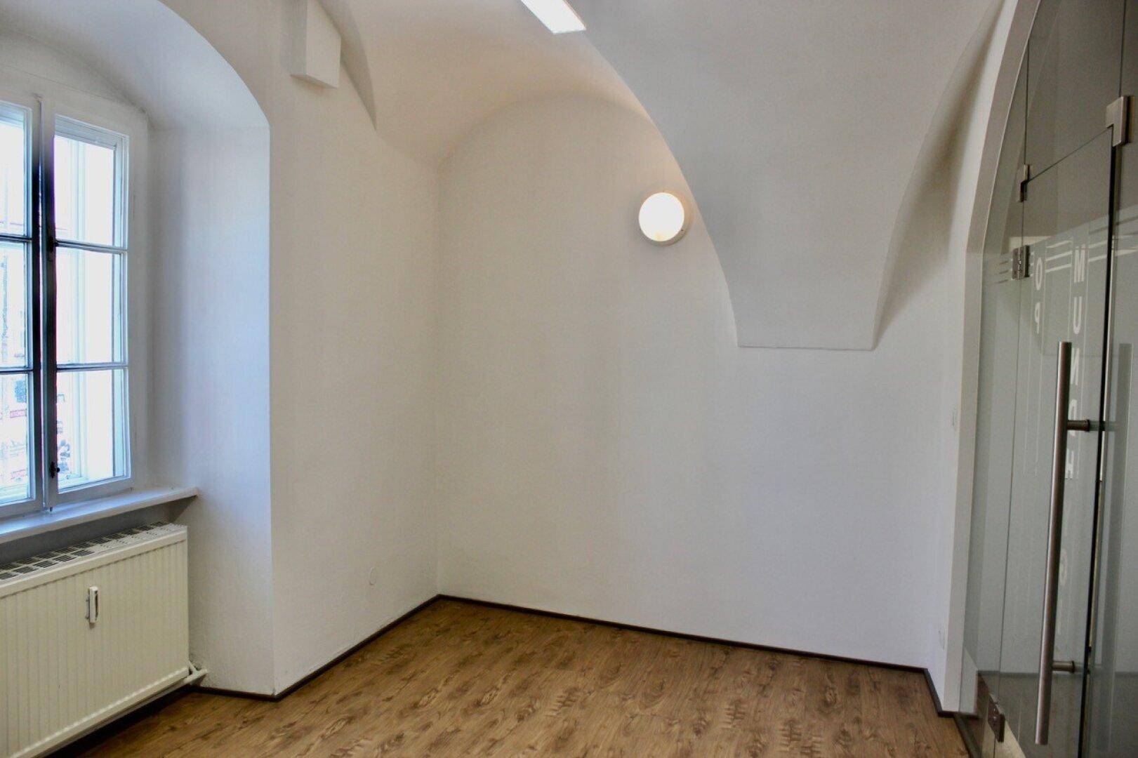 Raum mit gewölbter Decke, Fenster und moderner Glastür, bietet vielseitige Nutzungsmöglichkeiten.