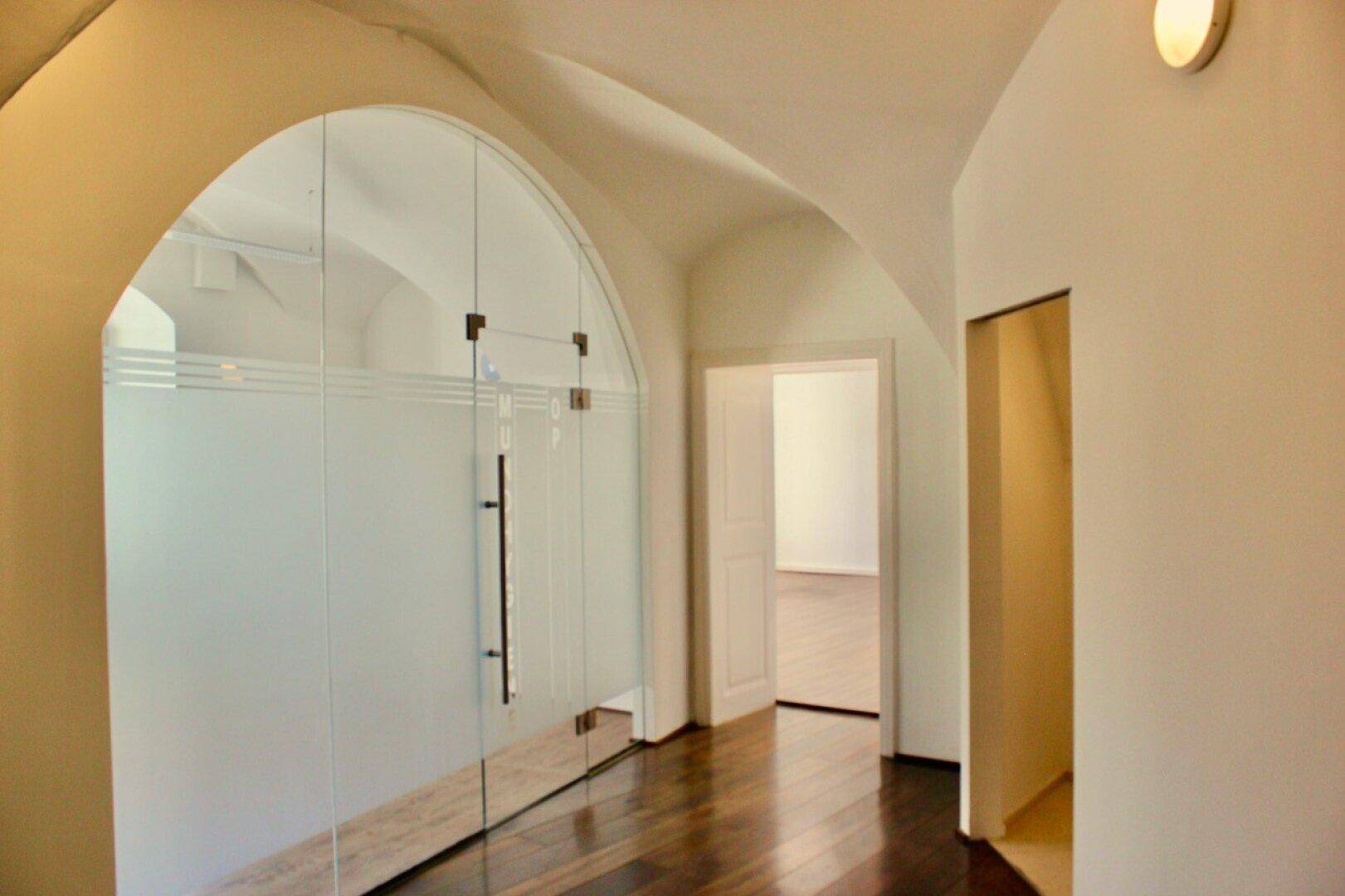 Flur mit gewölbter Decke, dunklem Holzboden und moderner Glastür, verbindet verschiedene Räume.