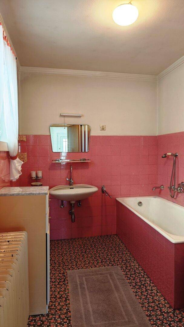 Badezimmer im Stil der 80er Jahre mit rosa Fliesen, Badewanne und Einzelwaschbecken.