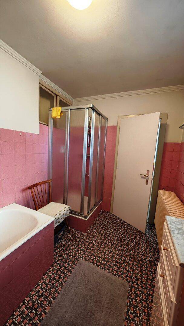 Badezimmer mit Duschkabine, Badewanne und rosa Fliesen im Retro-Stil.