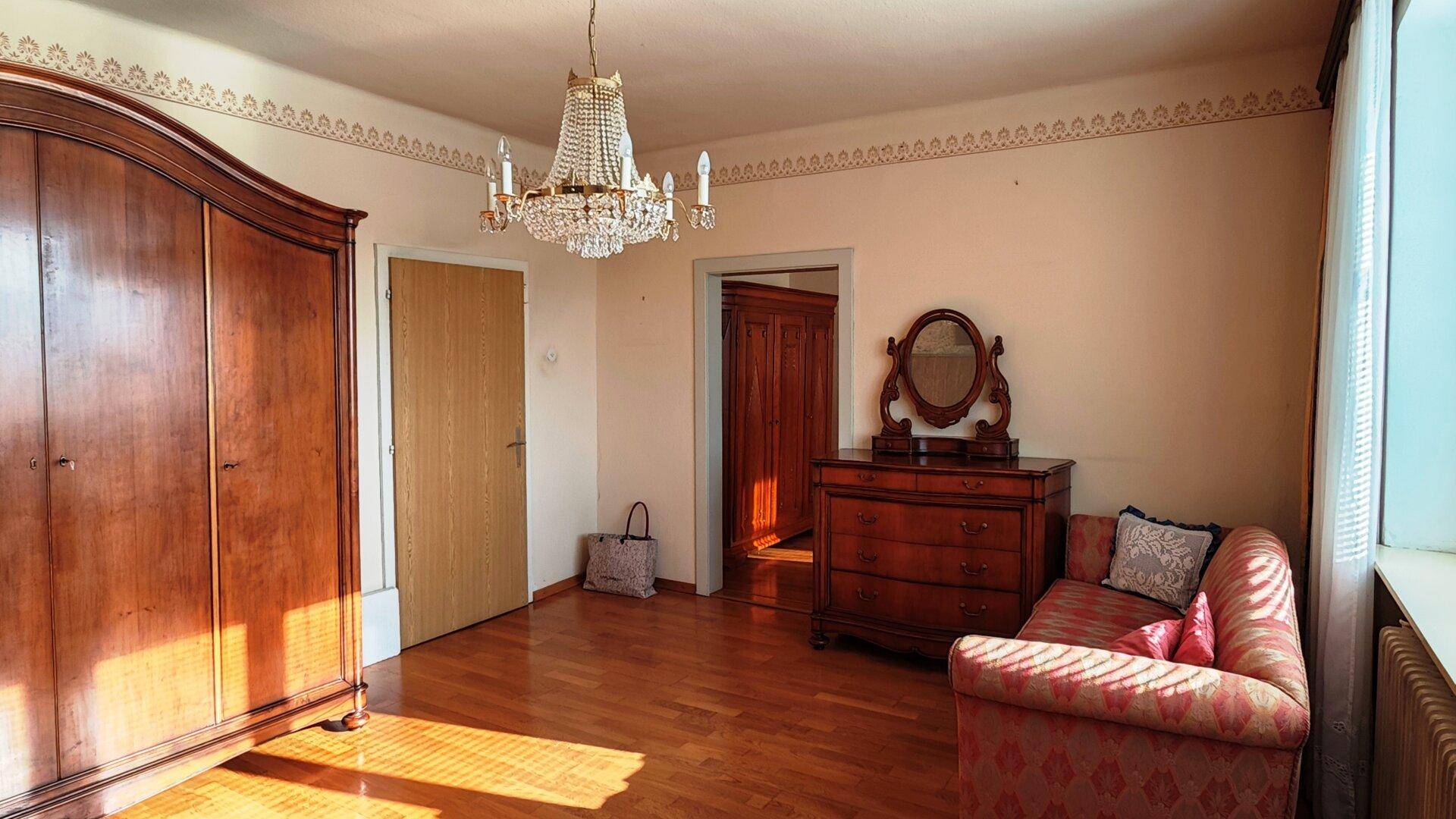 Schlafzimmer mit großem Holzschrank, Kommode und Kronleuchter, klassisch eingerichtet.
