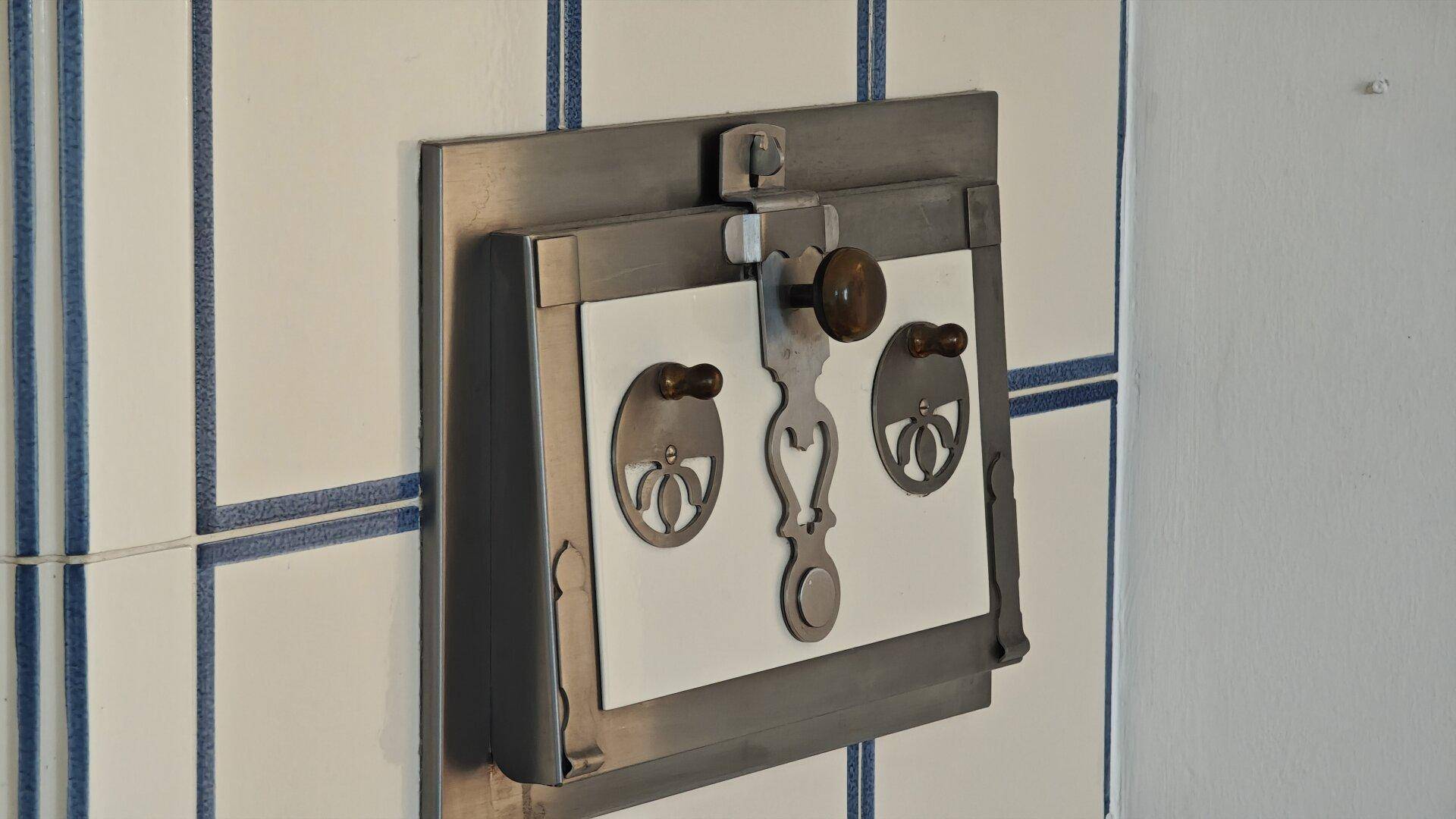 Detailaufnahme des traditionellen Kachelofens mit verzierten Metalltüren und blauen Fliesen.