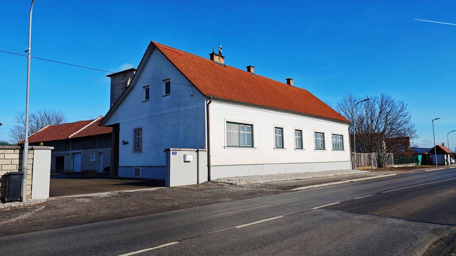 Seitenansicht des Hauses von der Straße aus mit rotem Ziegeldach und blauer Fassade.