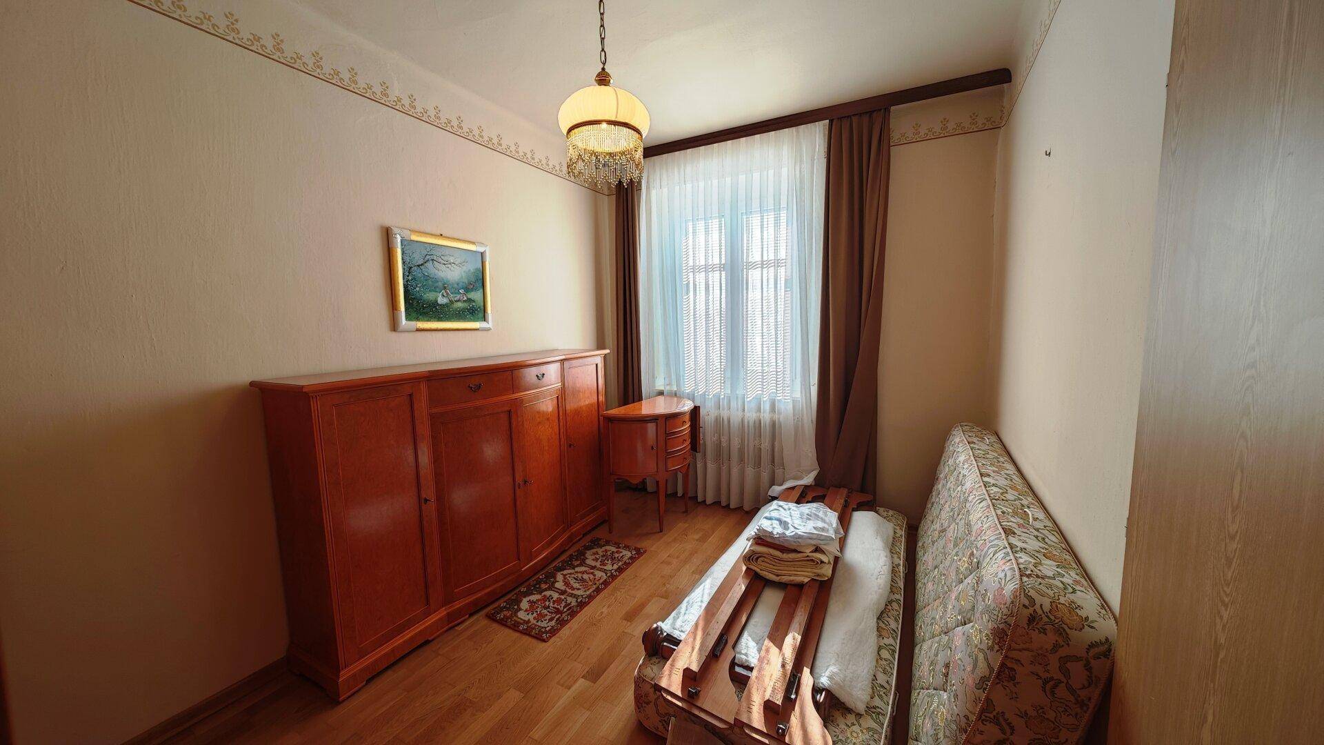 Gemütliches Schlafzimmer mit Einzelbett, Holzmöbeln und Fenster mit Vorhängen.
