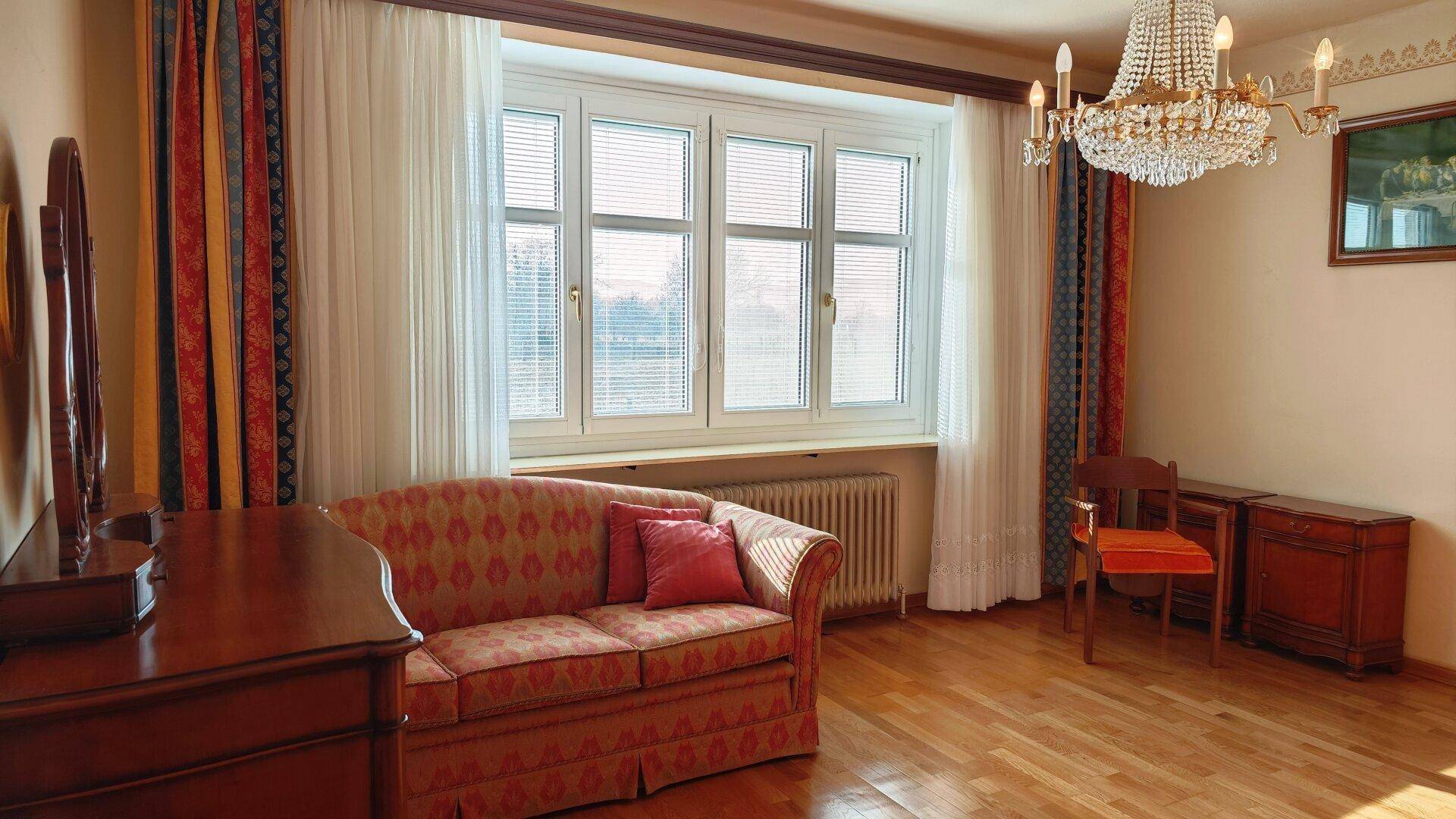 Helles Wohnzimmer mit klassischem Sofa, Kronleuchter und großen Fenstern.