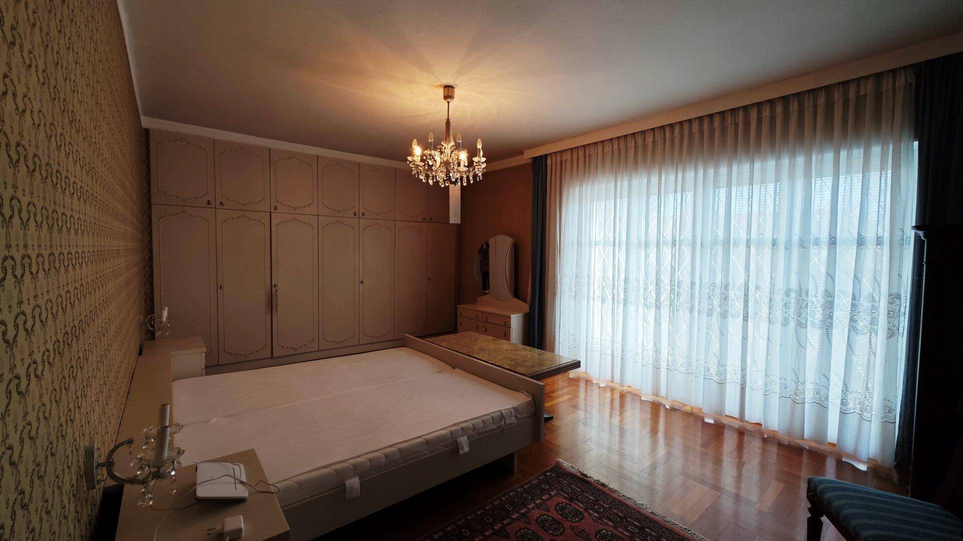 Großes Schlafzimmer mit Doppelbett, Einbauschränken und elegantem Kronleuchter.