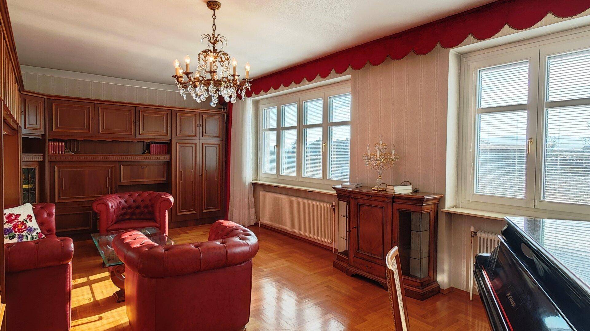 Geräumiges Wohnzimmer mit Klavier, roten Ledersesseln und elegantem Kronleuchter.