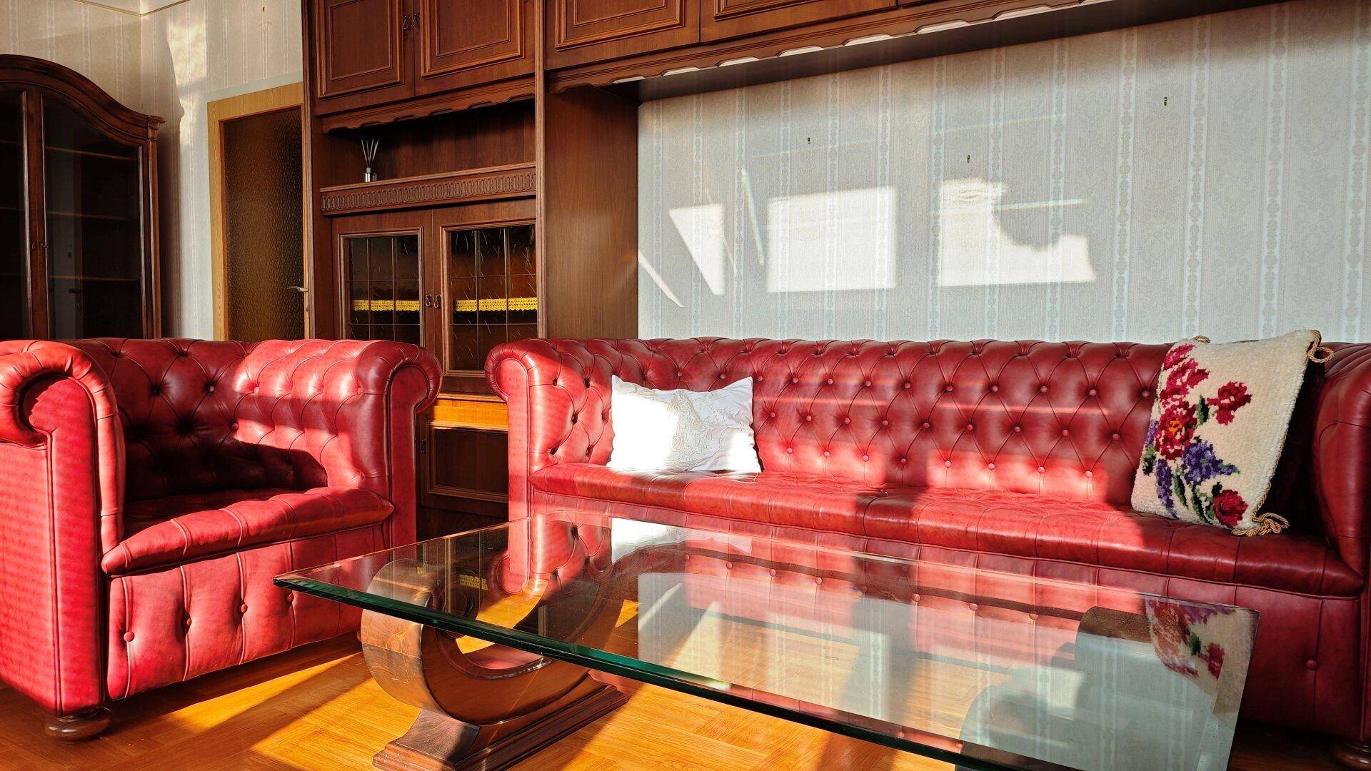 Elegantes Wohnzimmer mit roten Ledersofas, Glas-Couchtisch und Holzvertäfelung.