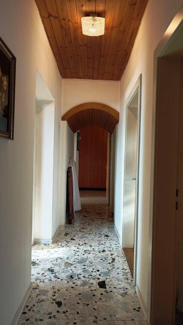 Langer Flur mit Holzdecke, gemustertem Boden und Durchgang zu weiteren Räumen.