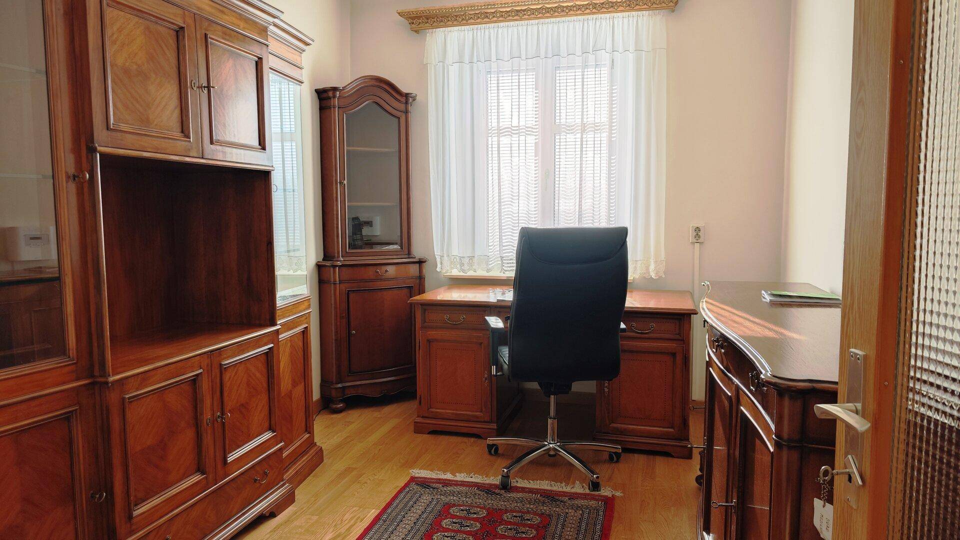 Klassisches Arbeitszimmer mit großem Holzschreibtisch, Bürostuhl und Bücherregalen.