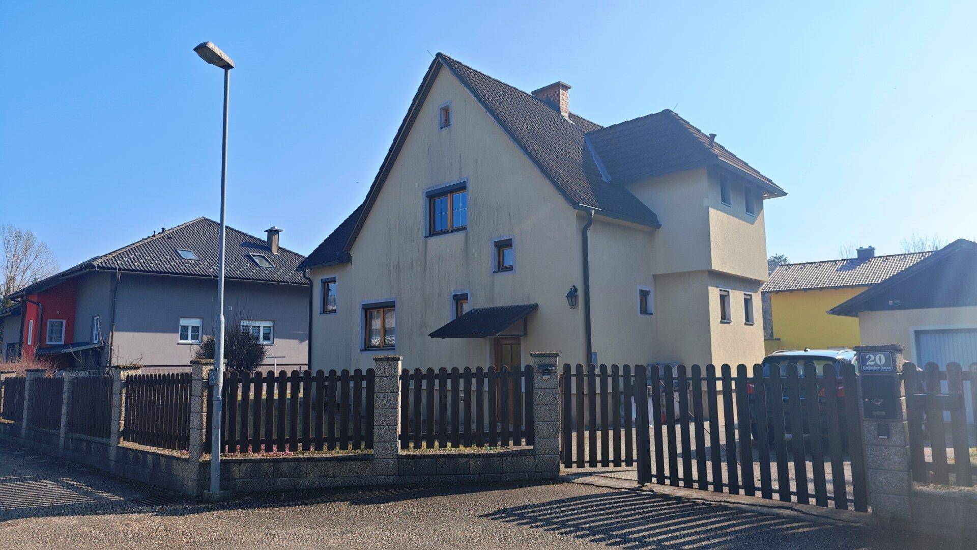 Vorderansicht des Einfamilienhauses mit Holzzaun und Zufahrt von der Straße.